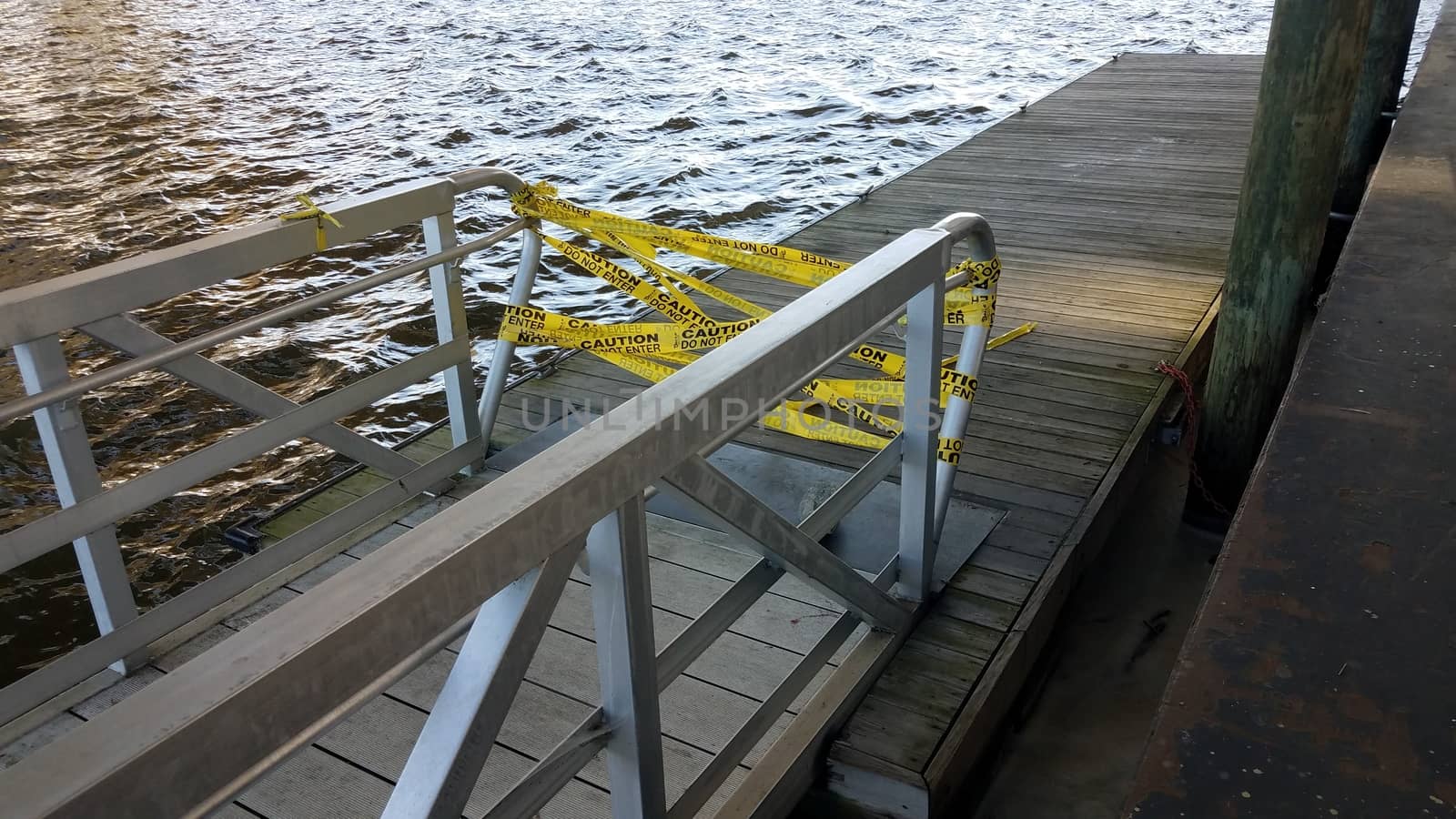 yellow cauton do not enter tape with wood pier and river water