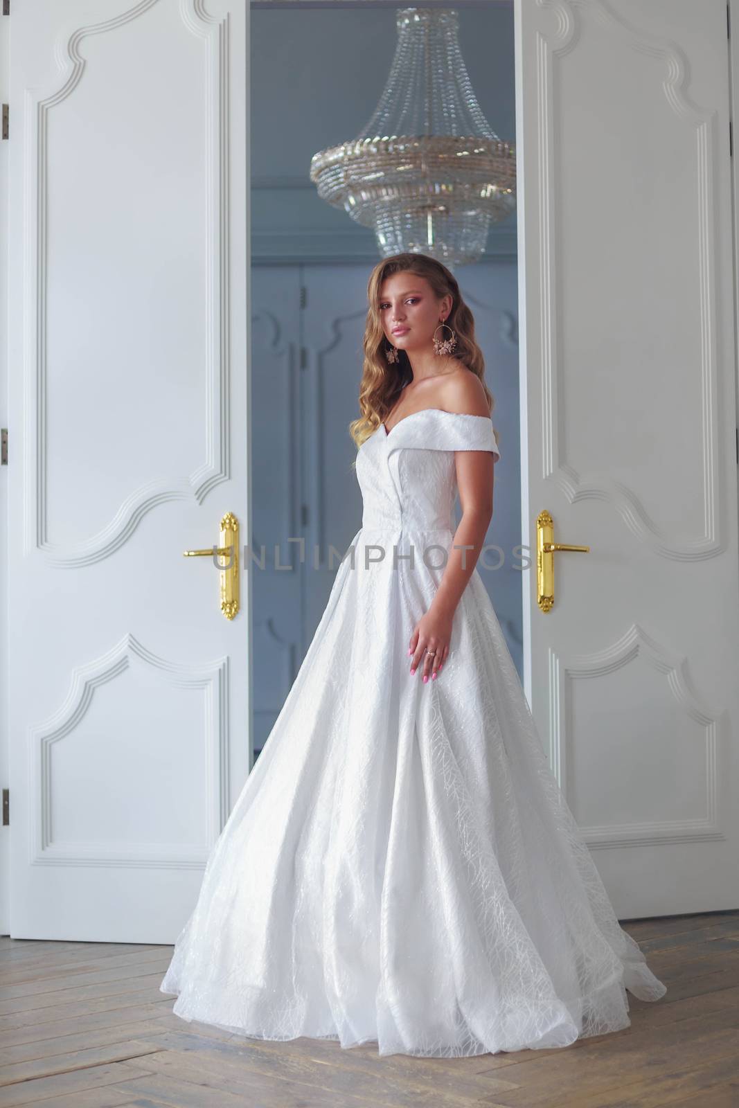 The bride stands at the door in a beautiful white room on the day of her wedding ceremony