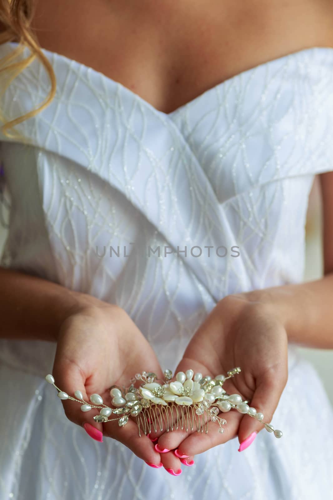 Close-up of bride's hands with hair ornament for wedding hairstyle.