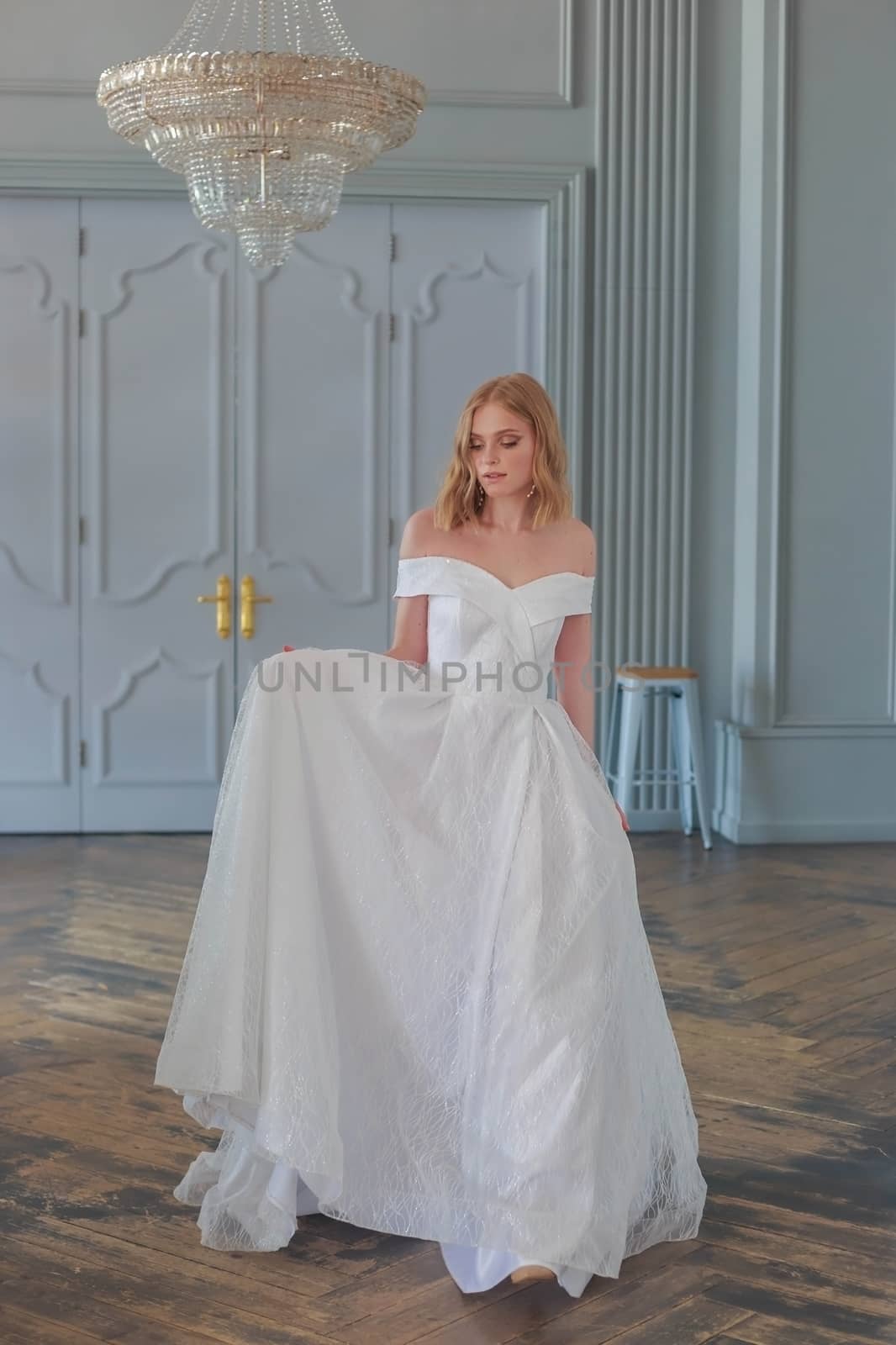 The bride in a beautiful white wedding dress enters the hall holding the hem of the dress