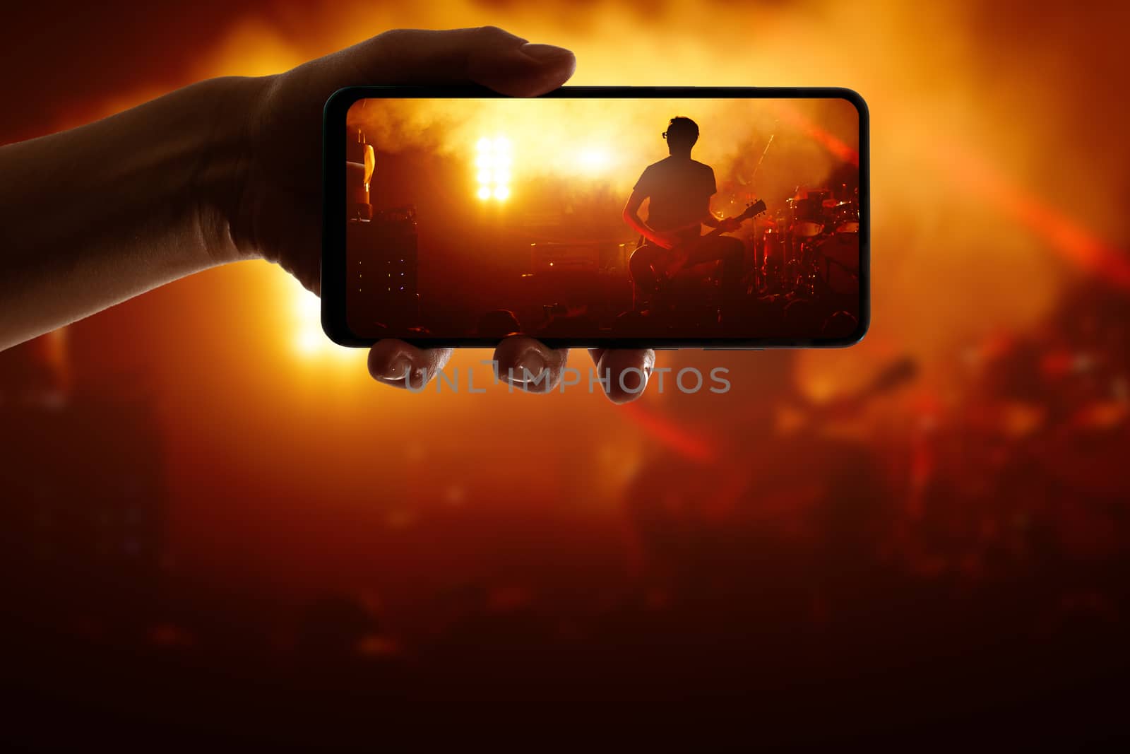 Hand with smartphone records live music concert. Using a mobile phone at the show