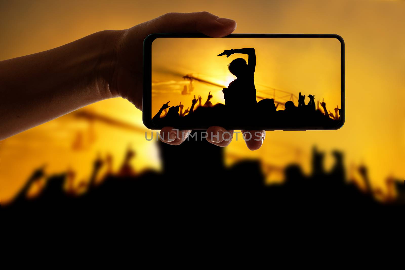 Silhouette of hand using camera phone to take pictures and videos at pop concert, festival by 9parusnikov