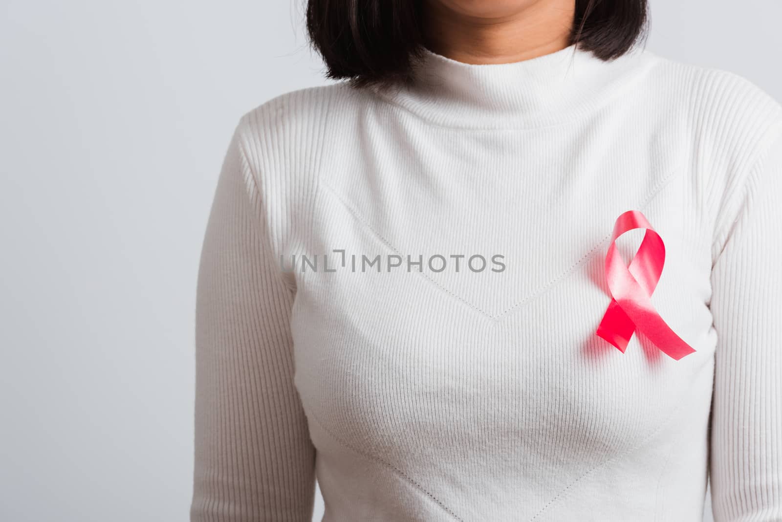 Breast cancer awareness healthcare and medicine concept. Close up Asian woman wear white shirt standing with pink breast cancer awareness ribbon pin on chest, studio shot isolated on white background