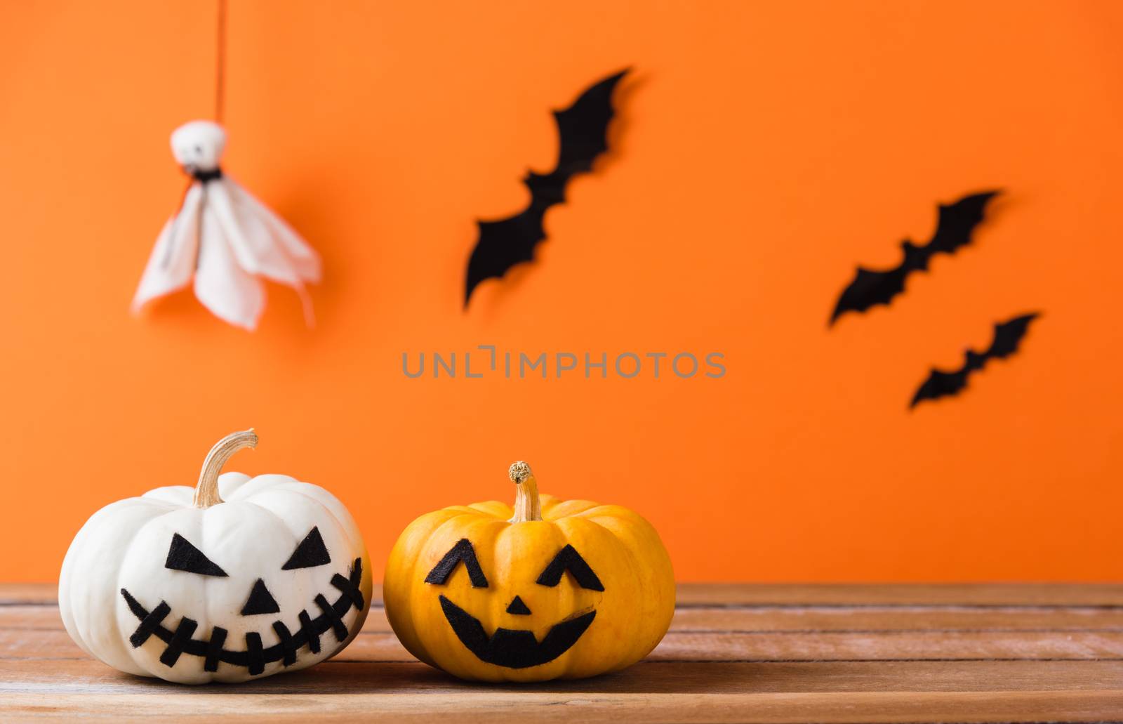 Funny Halloween day decoration party, Cute pumpkin ghost spooky jack o lantern face, black spider and bats on wooden table, studio shot isolated on an orange background, Happy holiday concept