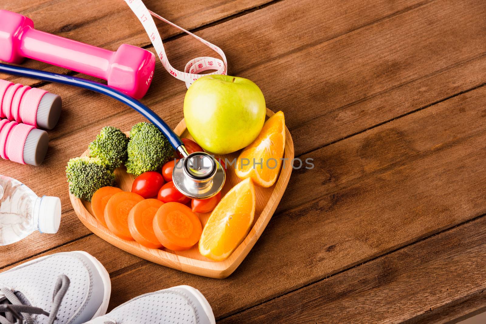 Top view of fresh fruits and vegetables in heart plate wood (apple, carrot, tomato, orange, broccoli) and sports equipment and doctor stethoscope on wooden table, Healthy lifestyle diet food concept