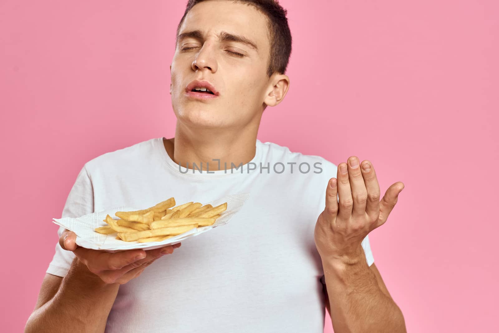 Man with French fries in a paper box on a pink background calories fast food portrait pink background. High quality photo