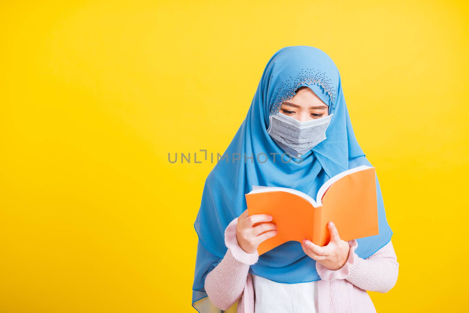 Asian Muslim Arab, Portrait of happy beautiful young woman religious wear veil hijab and face mask protective to prevent coronavirus she hold book on hand and open reding it on yellow, Back to college