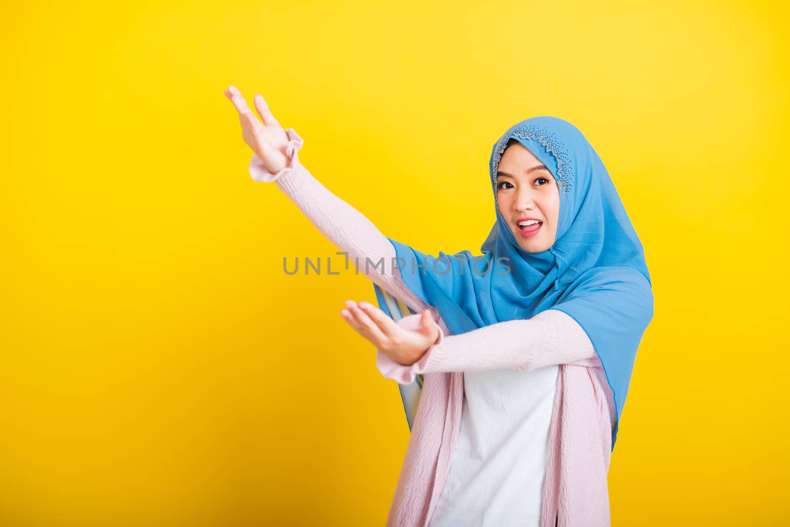 Asian Muslim Arab, Portrait of happy beautiful young woman Islam religious wear veil hijab funny smile she open arms for hug or raise hand to pick up items receive something from above isolated yellow