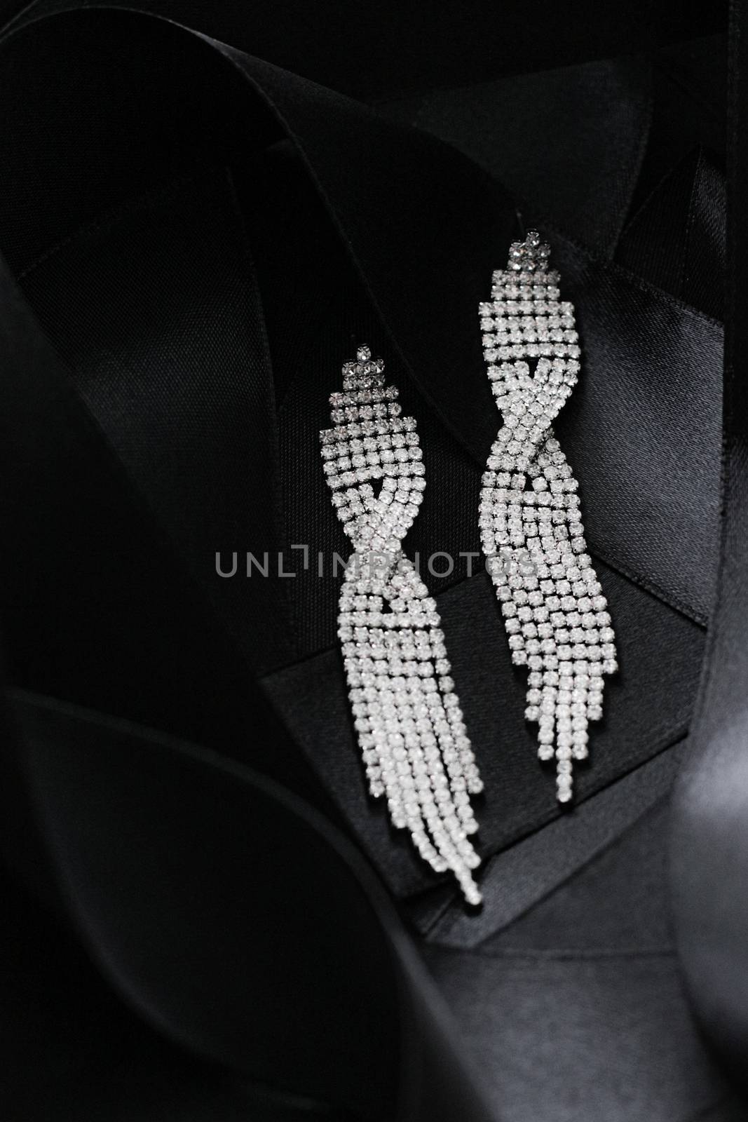 Luxury diamond earrings on black silk ribbon as background, jewelry and fashion brands