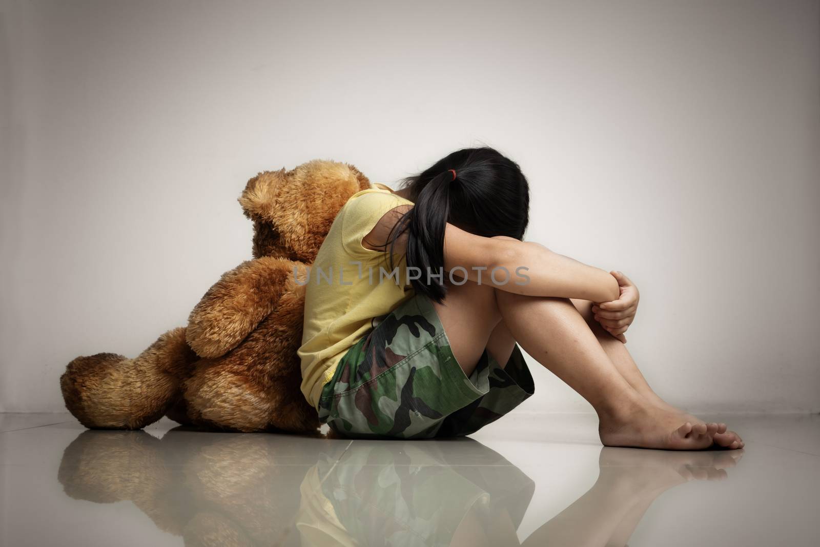 Little girl with teddy bear sitting on floor at empty room. Mental and depressed family concept. Back view