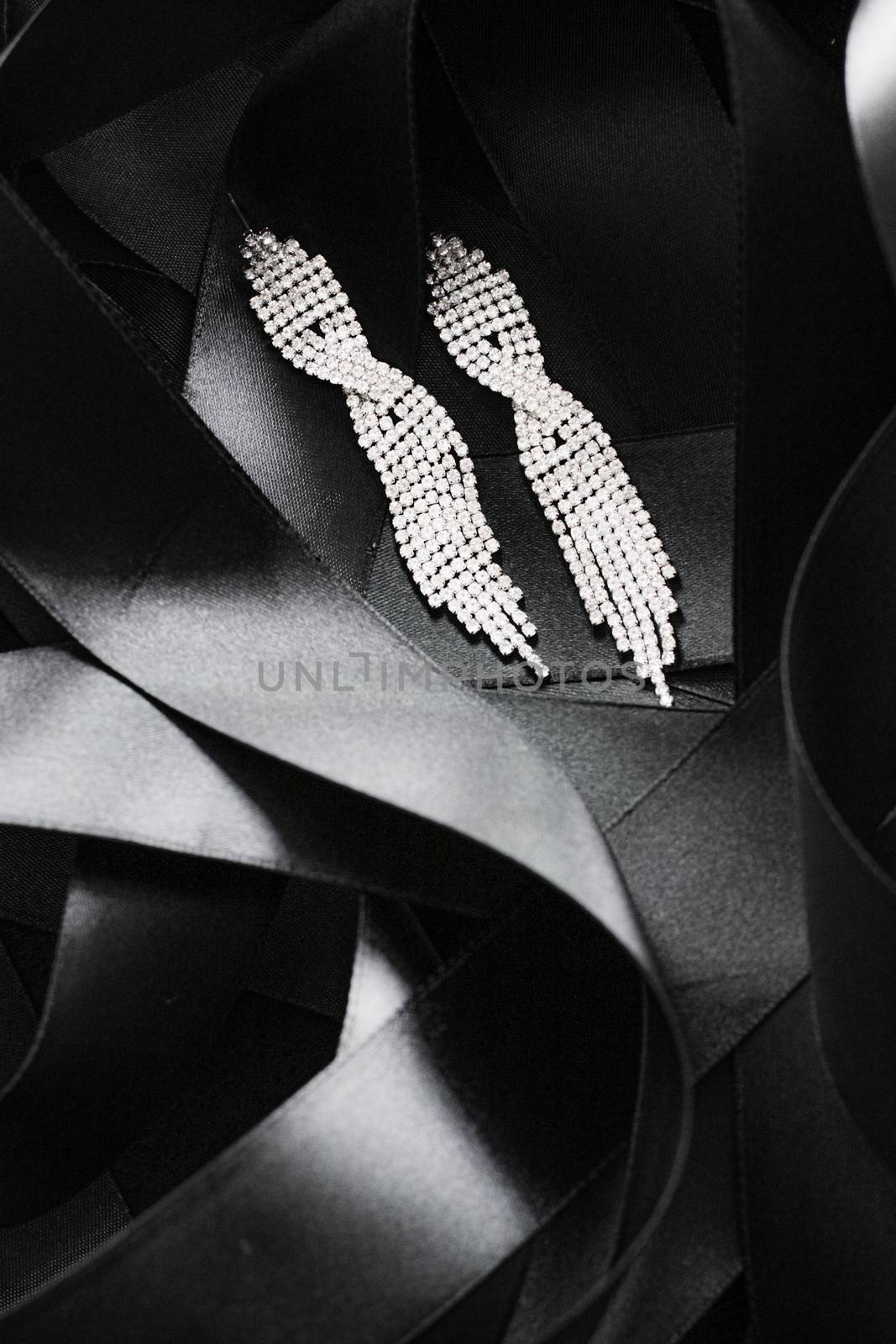 Luxury diamond earrings on black silk ribbon as background, jewelry and fashion brand by Anneleven