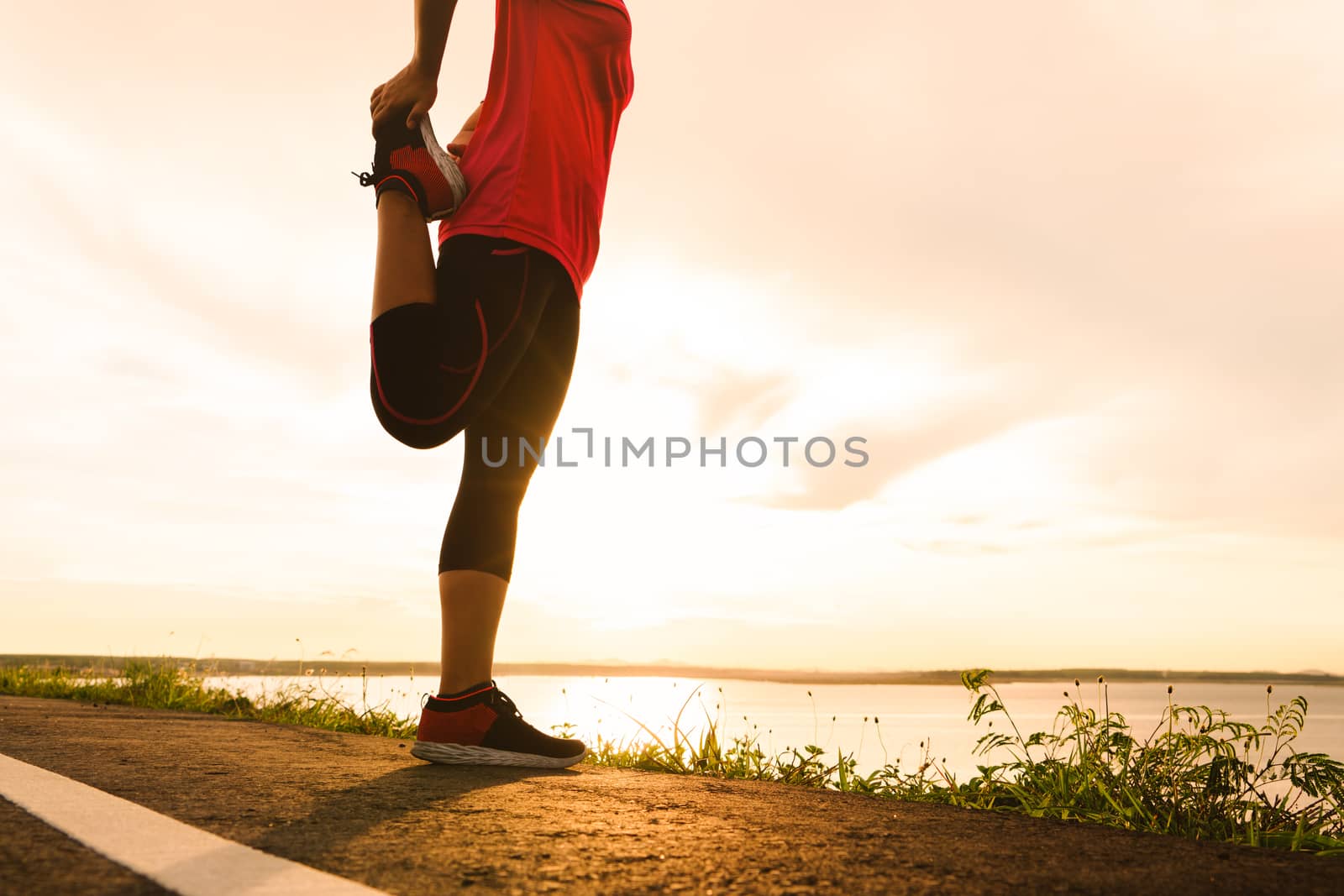 woman stretching leg muscle preparing for sunset trail run