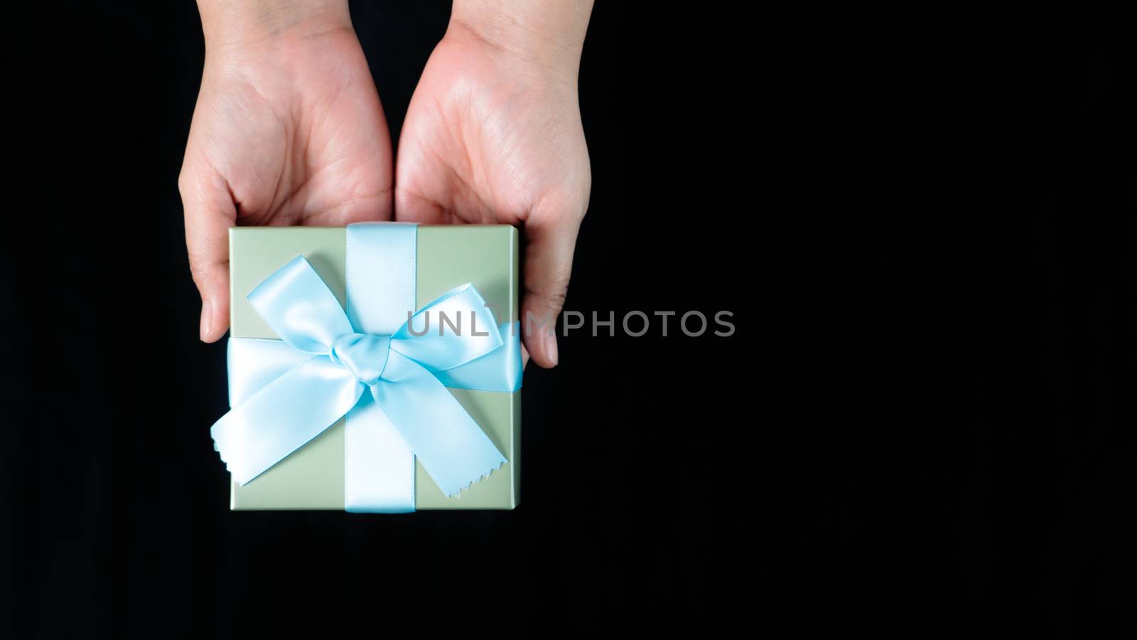 female hands holding a small gift wrapped with blue ribbon on black background