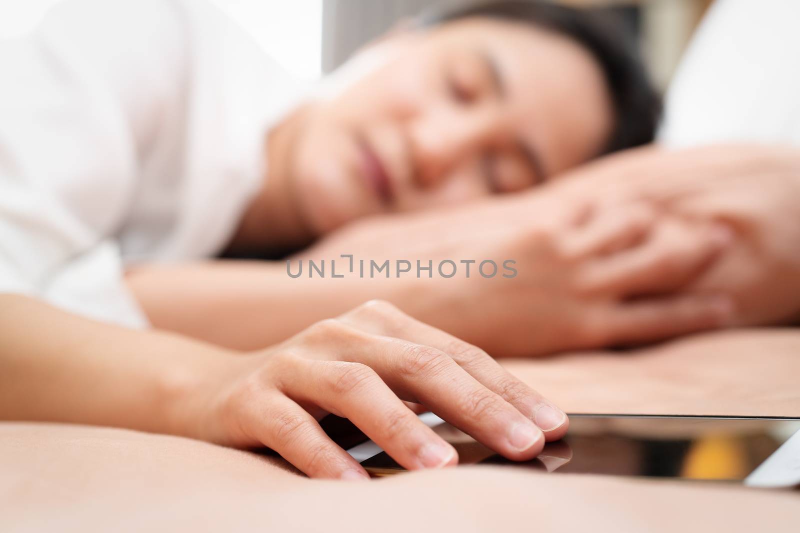 young woman holding hand on smartphone while sleeping in bed