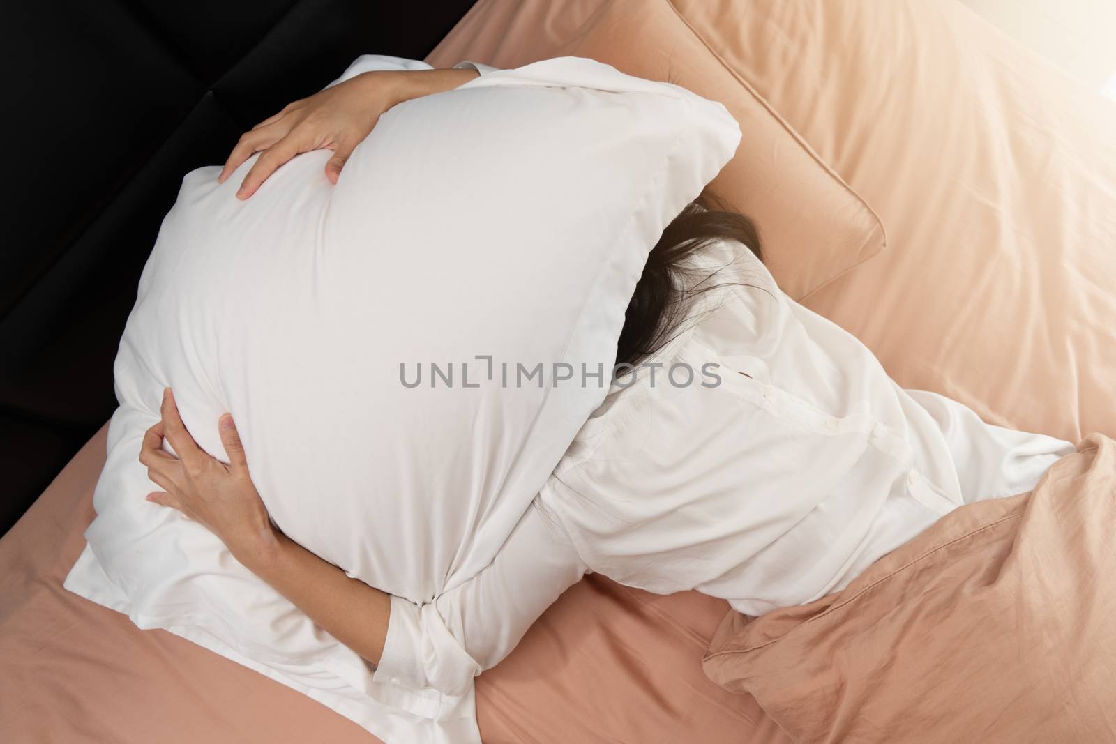 Sleepy woman hide under the pillow hates waking up early in the morning