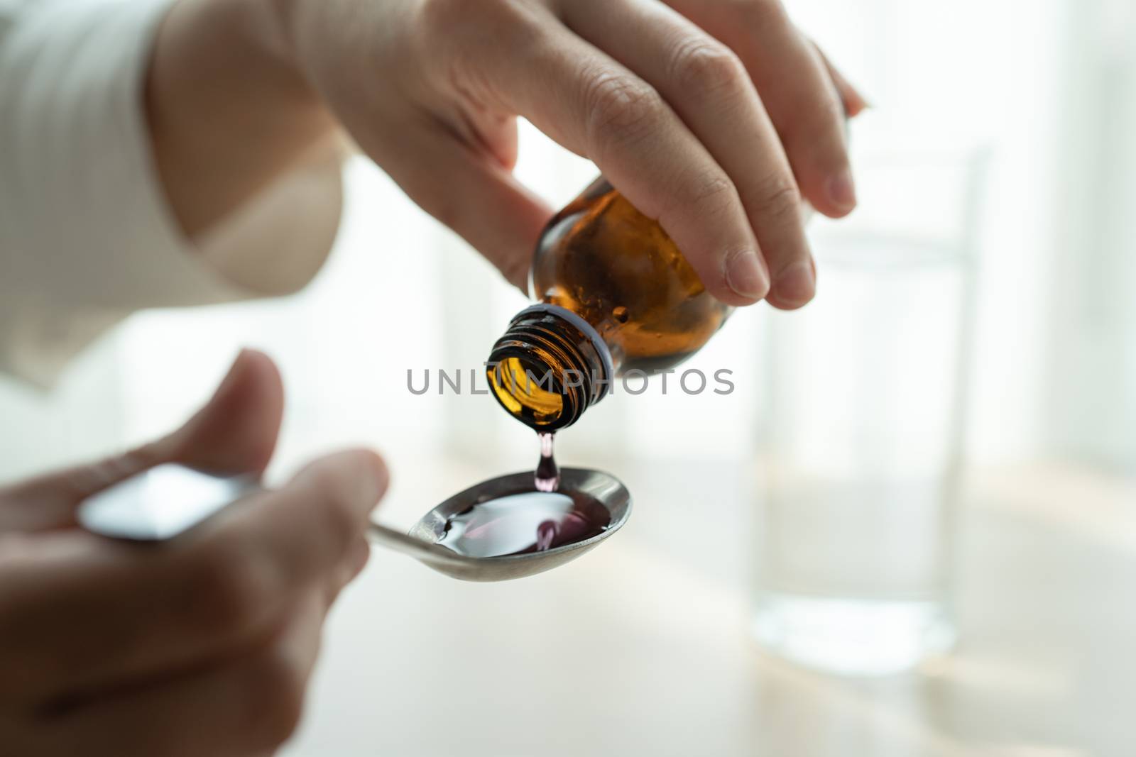Woman hand pouring medication or cough syrup from bottle to spoo by psodaz