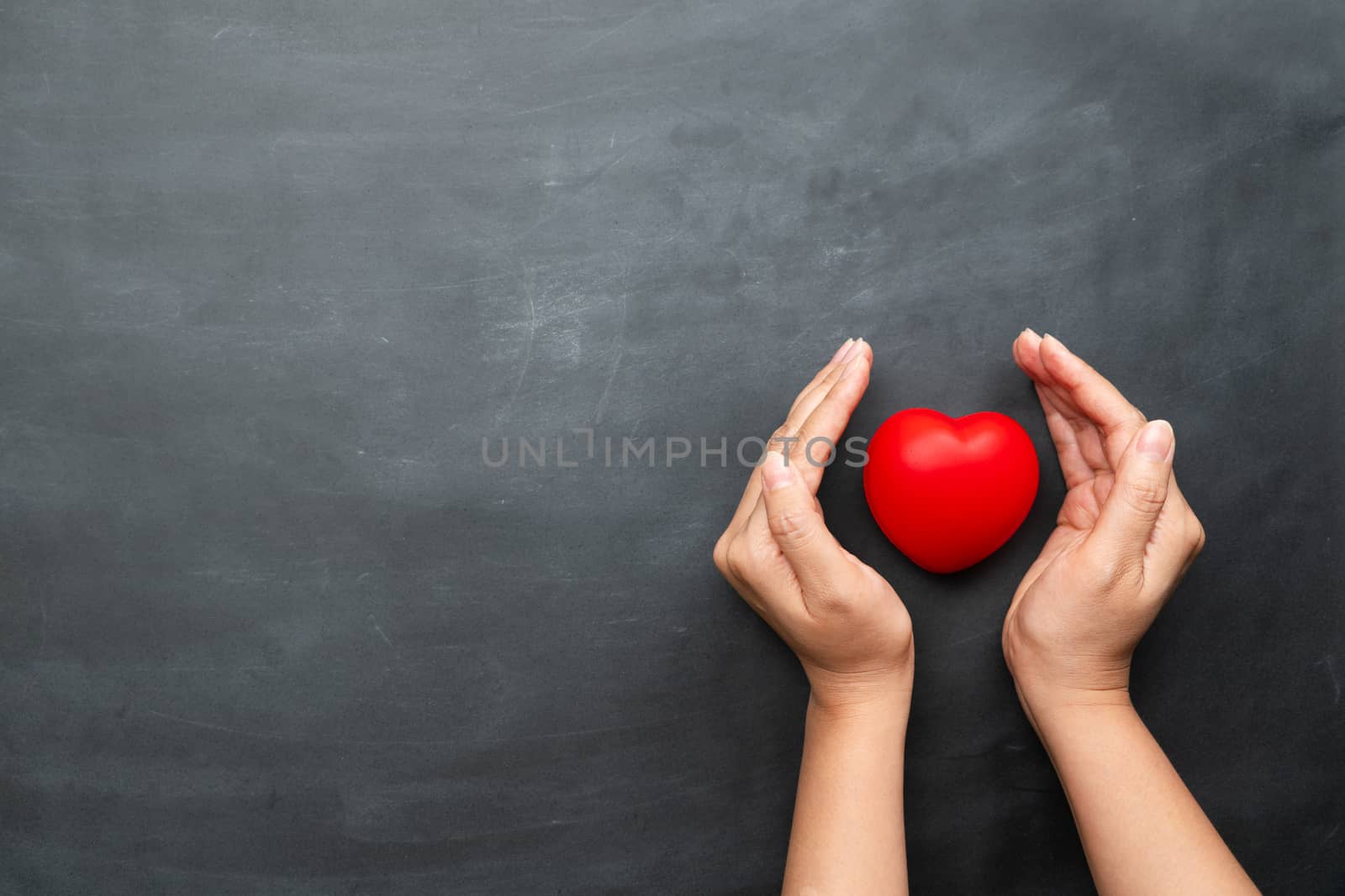 World heart day concept of young woman hand protecting red heart on black background