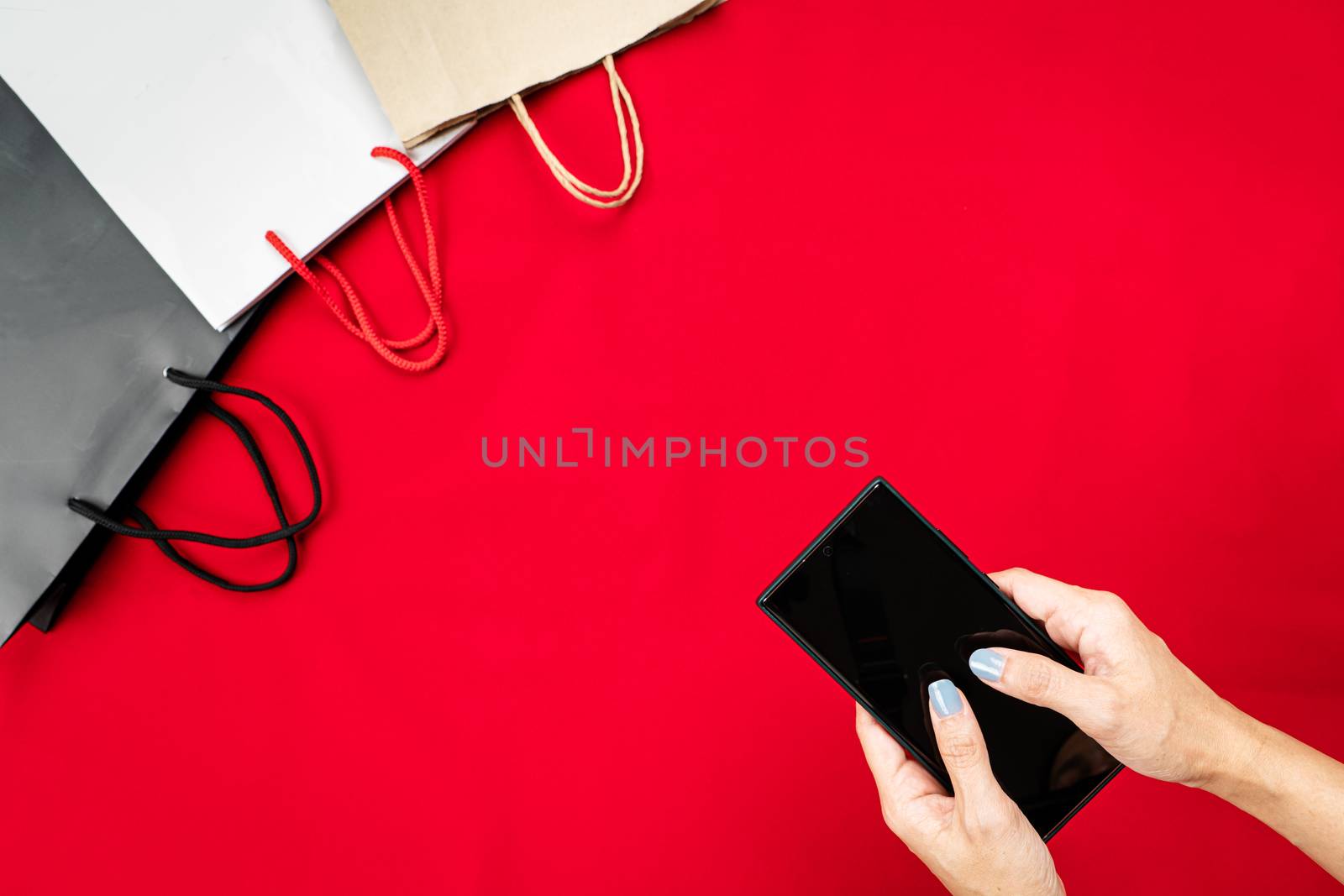 black friday sale, woman hand online shopping on smartphone with shopping bag on red background