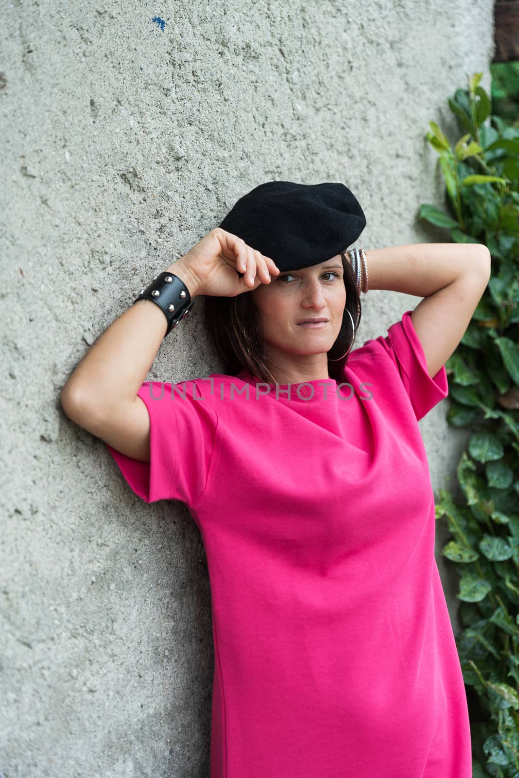 girl with dark hair posing wearing a black beret and a fuchsia dress and a bracelet, image of a woman posing in front of a light wall