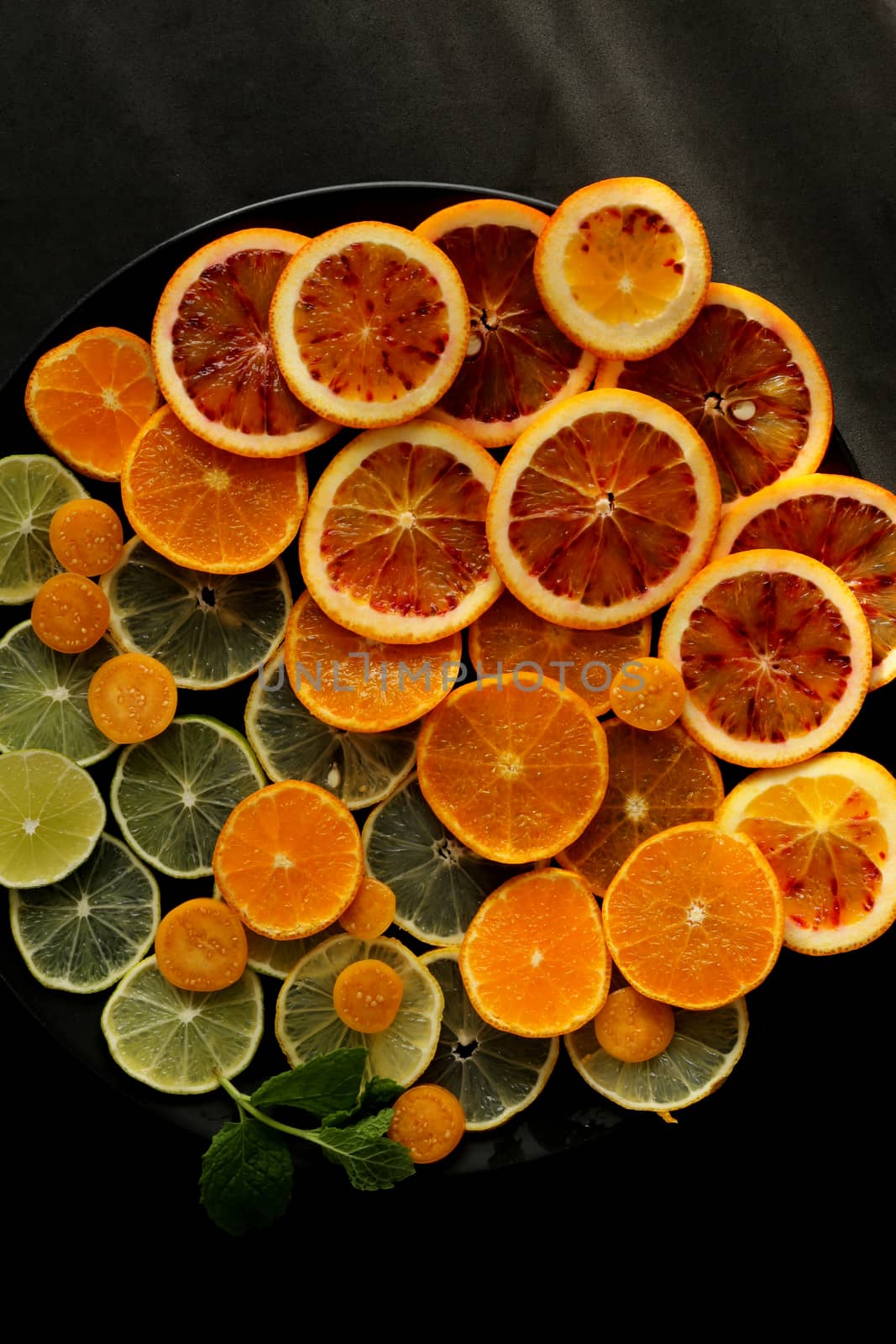 fresh slices of citrus fruits on black round plate on black background. Sours of vitamin C, healthy life concept, vibrant color concept. Top view, flat lay