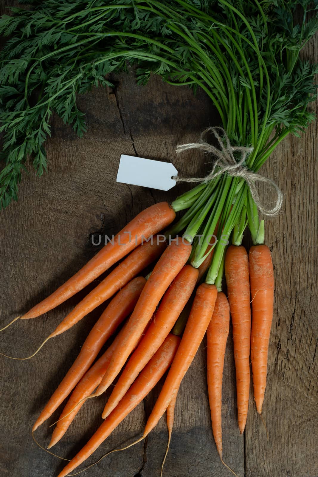 Fresh organic carrots with tag on antique wooden table. Rustic kitchen concept. Banner, poster, mock up. Grunge, vintage, rustic style