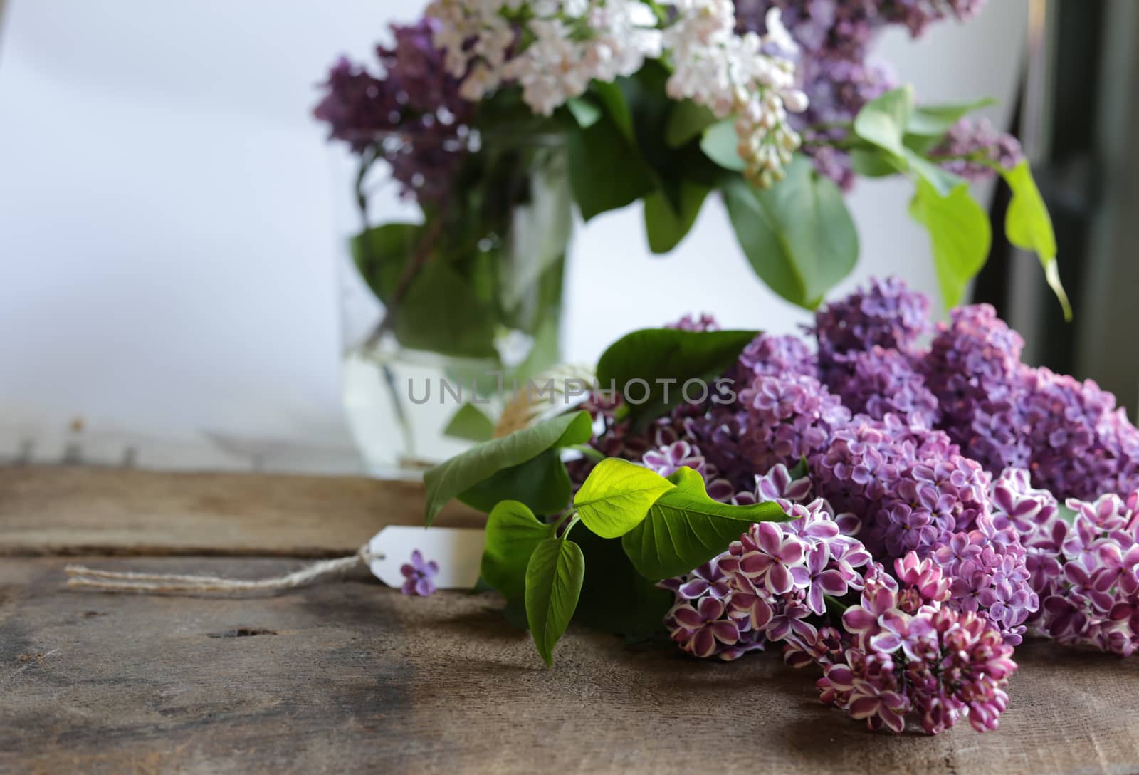 beautiful purple spring flowers with gift tag. Lilac flowers on old antique brown wood rustic background. Top view, flat lay. by NelliPolk