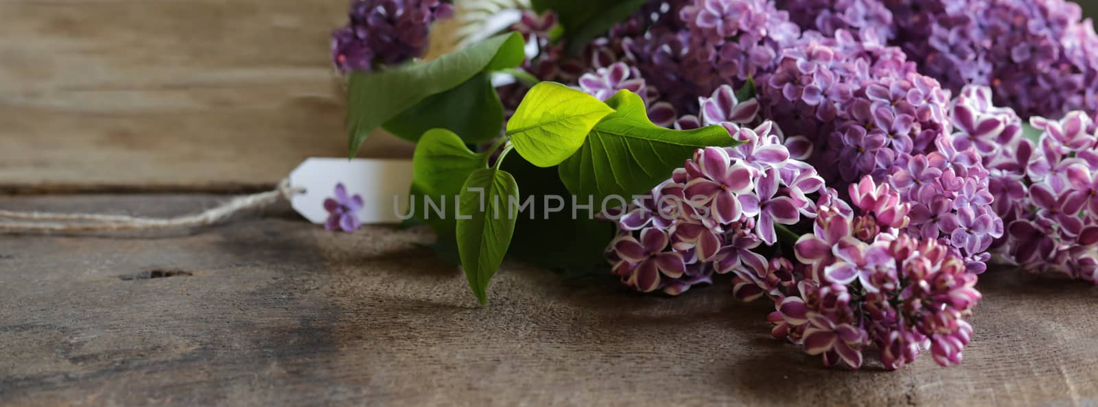 Happy mothers day beautiful purple spring flowers with gift tag. Lilac flowers on old antique brown wood rustic background. Top view, flat lay. Banner, card, poster concept.