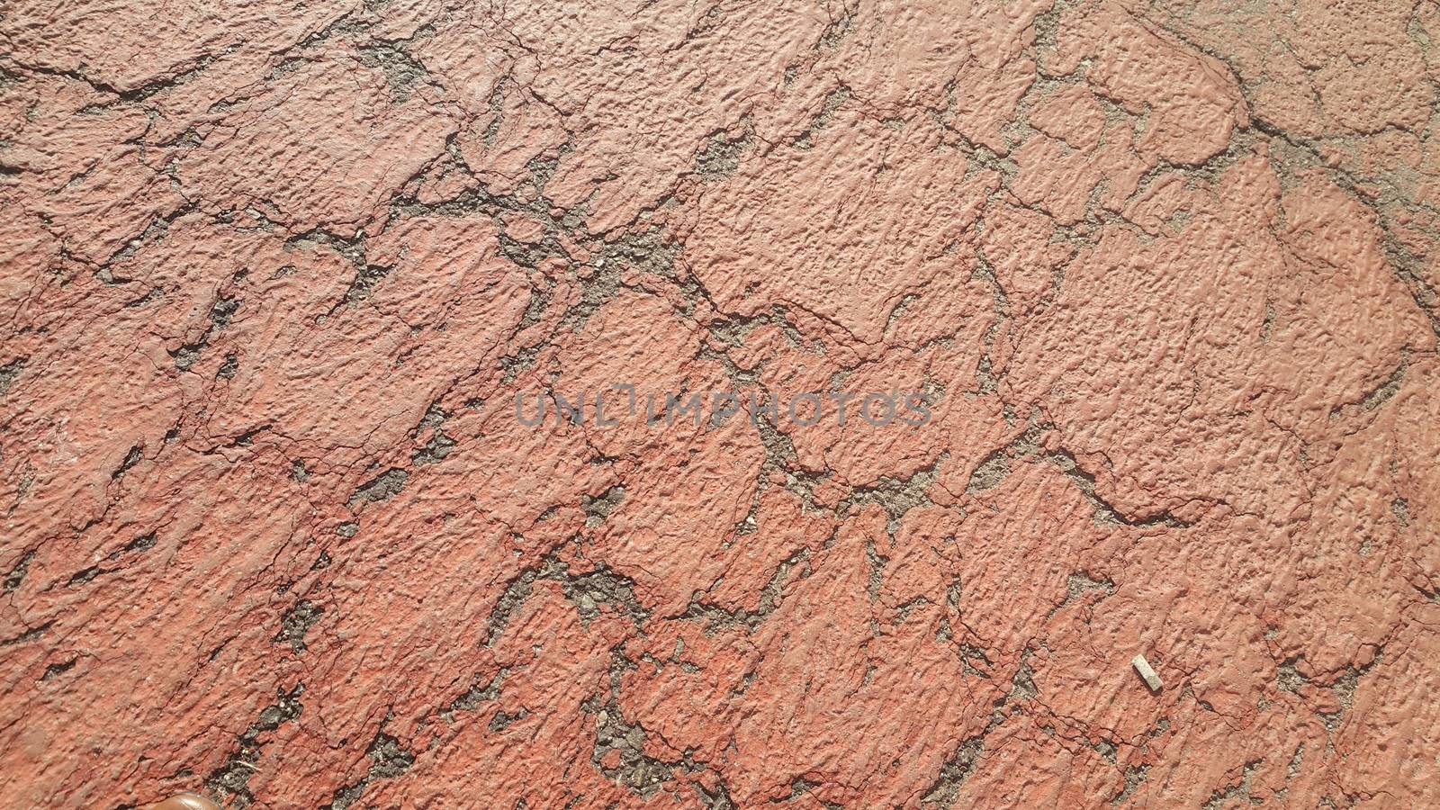 Red colored damaged road or paved pathway with crackes of different shpaes. Cracked texture with copy space for text and messages