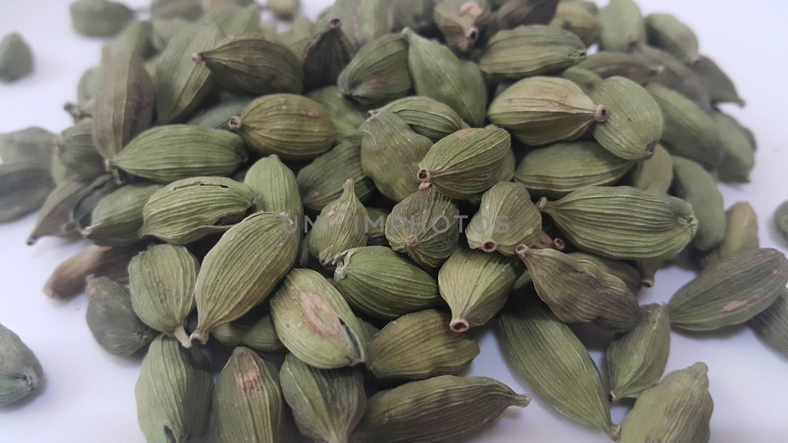 Closeup top view of dried green Elettaria cardamomum fruits with seeds, cardamom spice scattered on white background