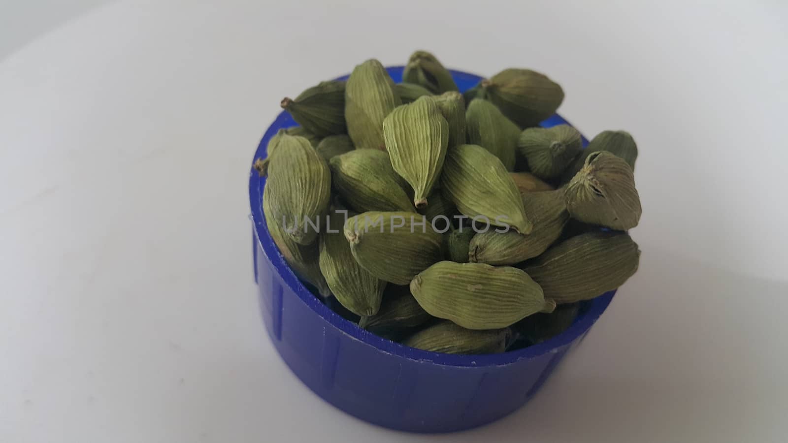 Closeup top view of dried green Elettaria cardamomum fruits with seeds, cardamom spice in small bowl on white background