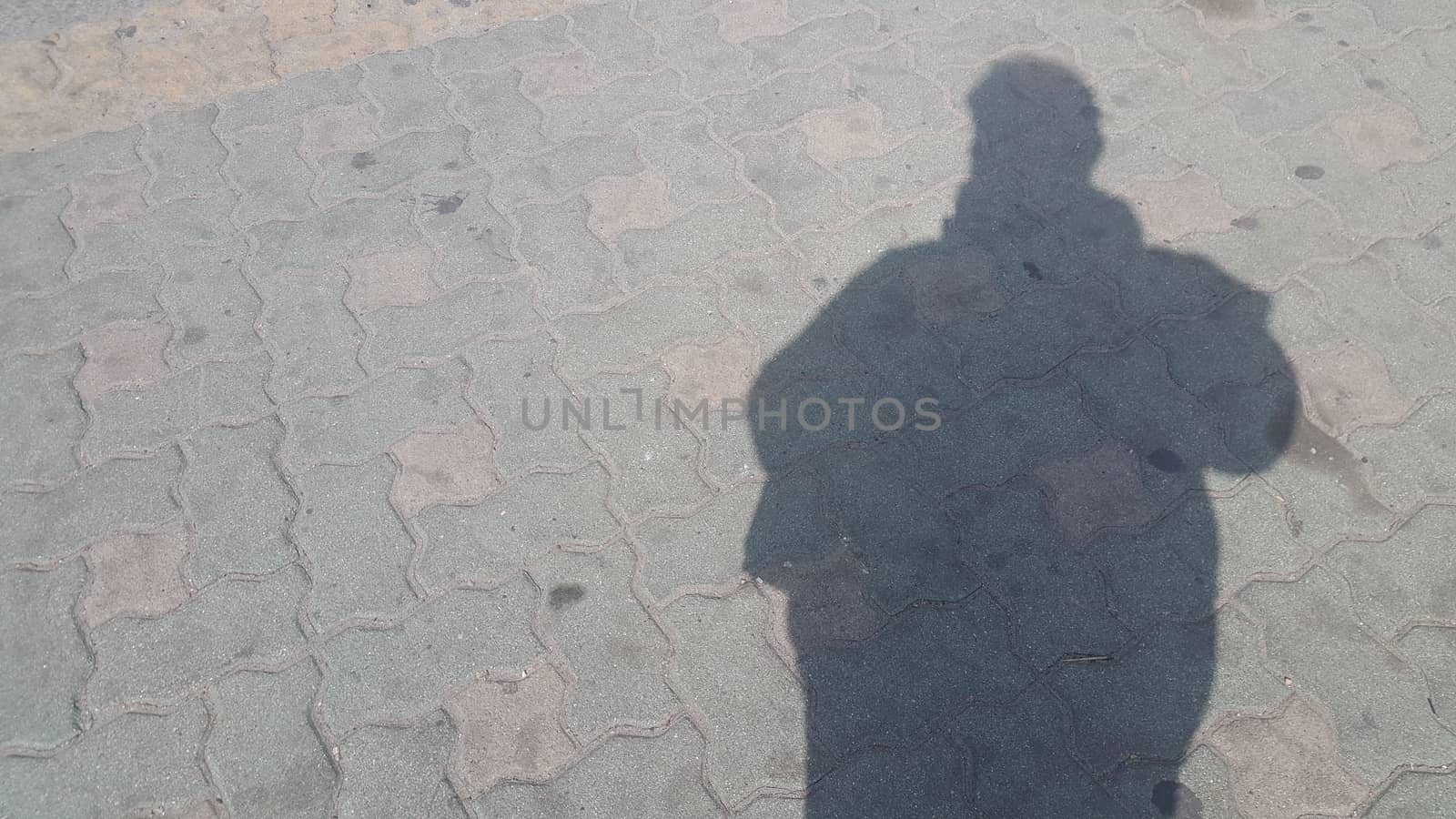 Silhouette: A Man's shadow on the red colored concrete ground under sunlight