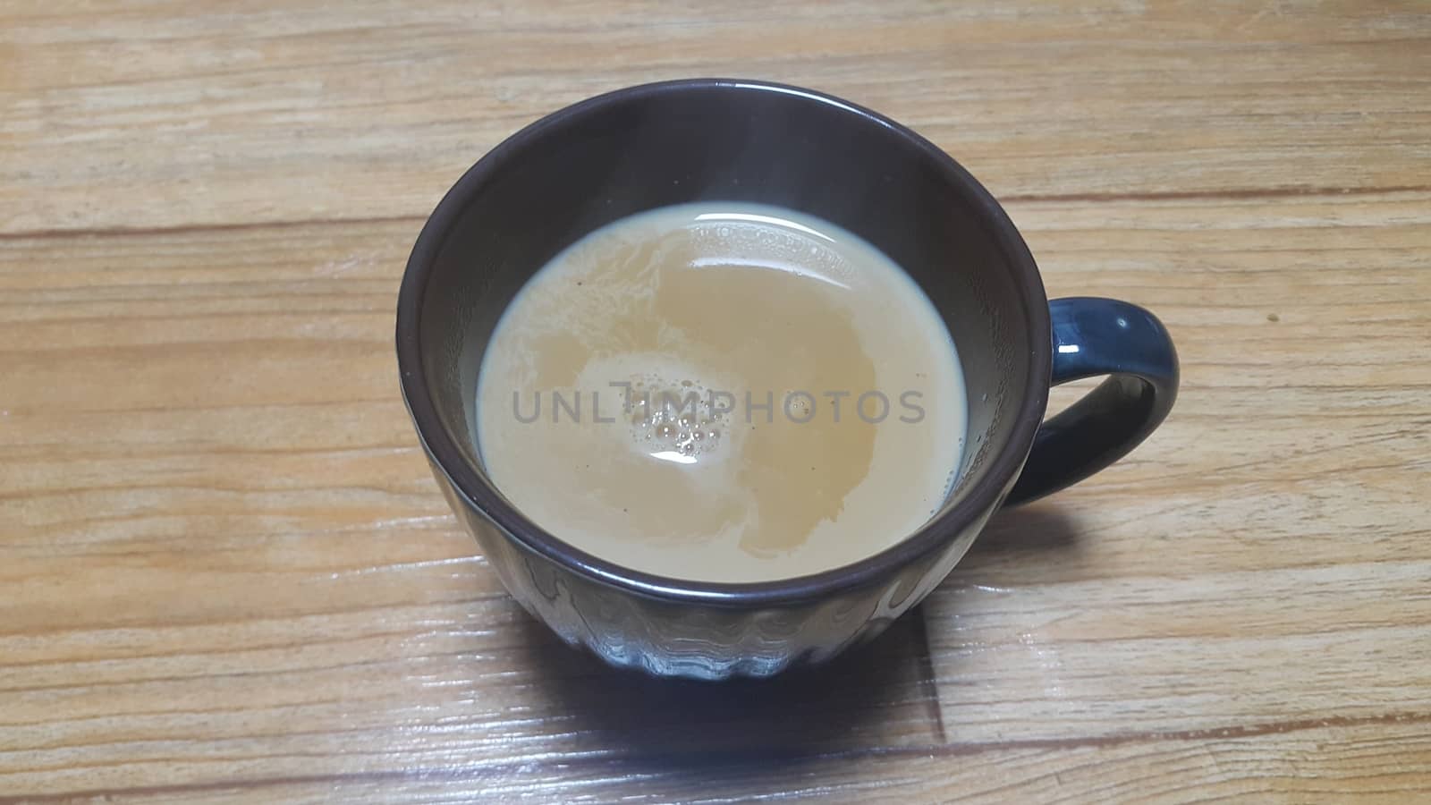 Top view of hot milk tea or black tea in a dark brown ceramic cup placed over a wooden floor.