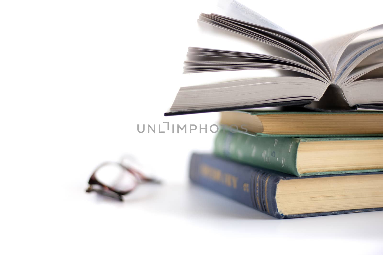 Open book on the pile of old books and reading glasses on white background. Time away from technology. Finding quiet place to calm the brain.