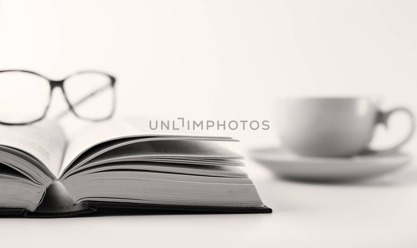 Open book, cup of tea coffee in soft focus and reading glasses on white background. Stay at home, freelance, learning from home concept