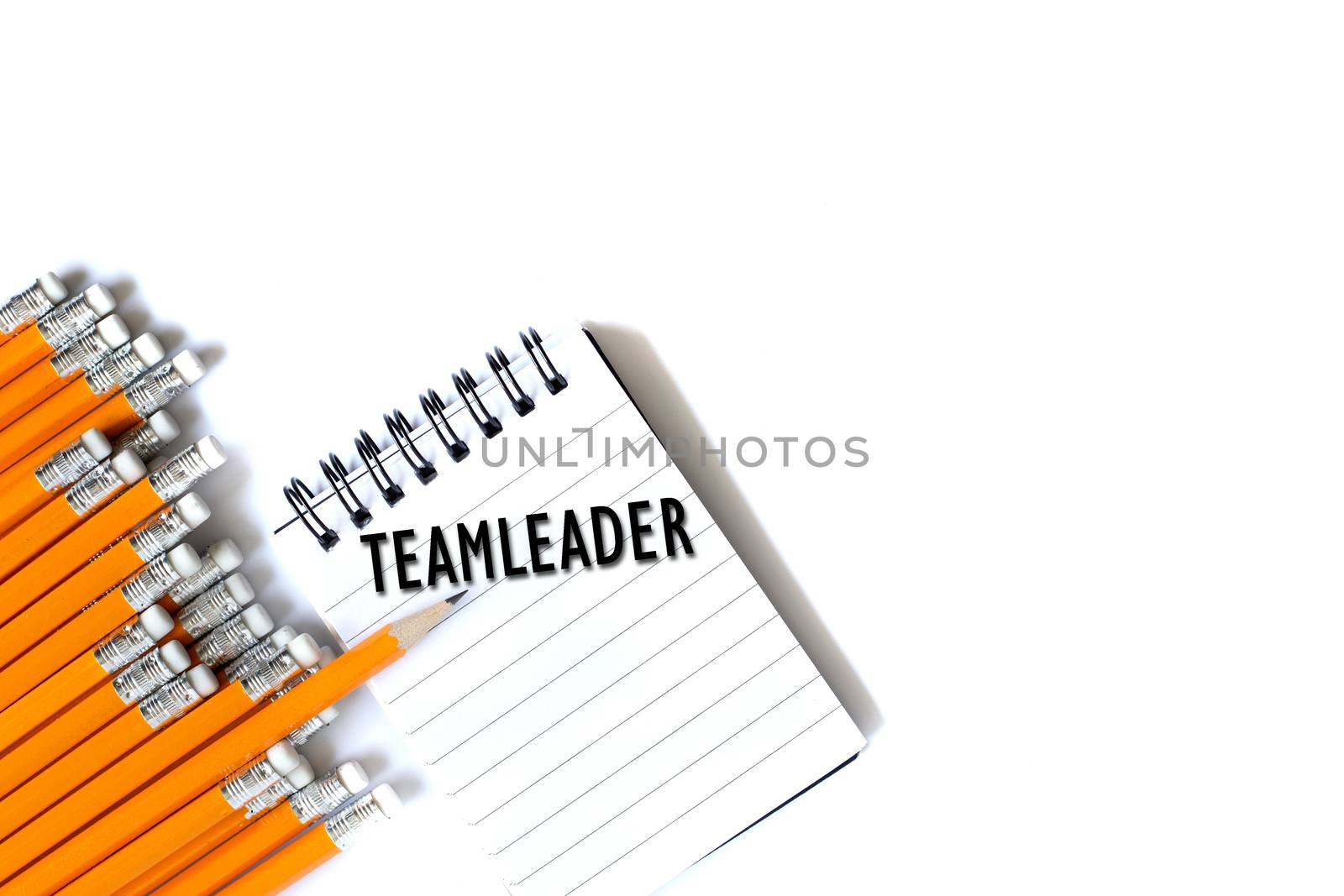 Sharp pencil in row of dull pencils standing out and word Teamleader on notebook. Flat lay from above on white background. Business concept of disruption, leadership or think differently