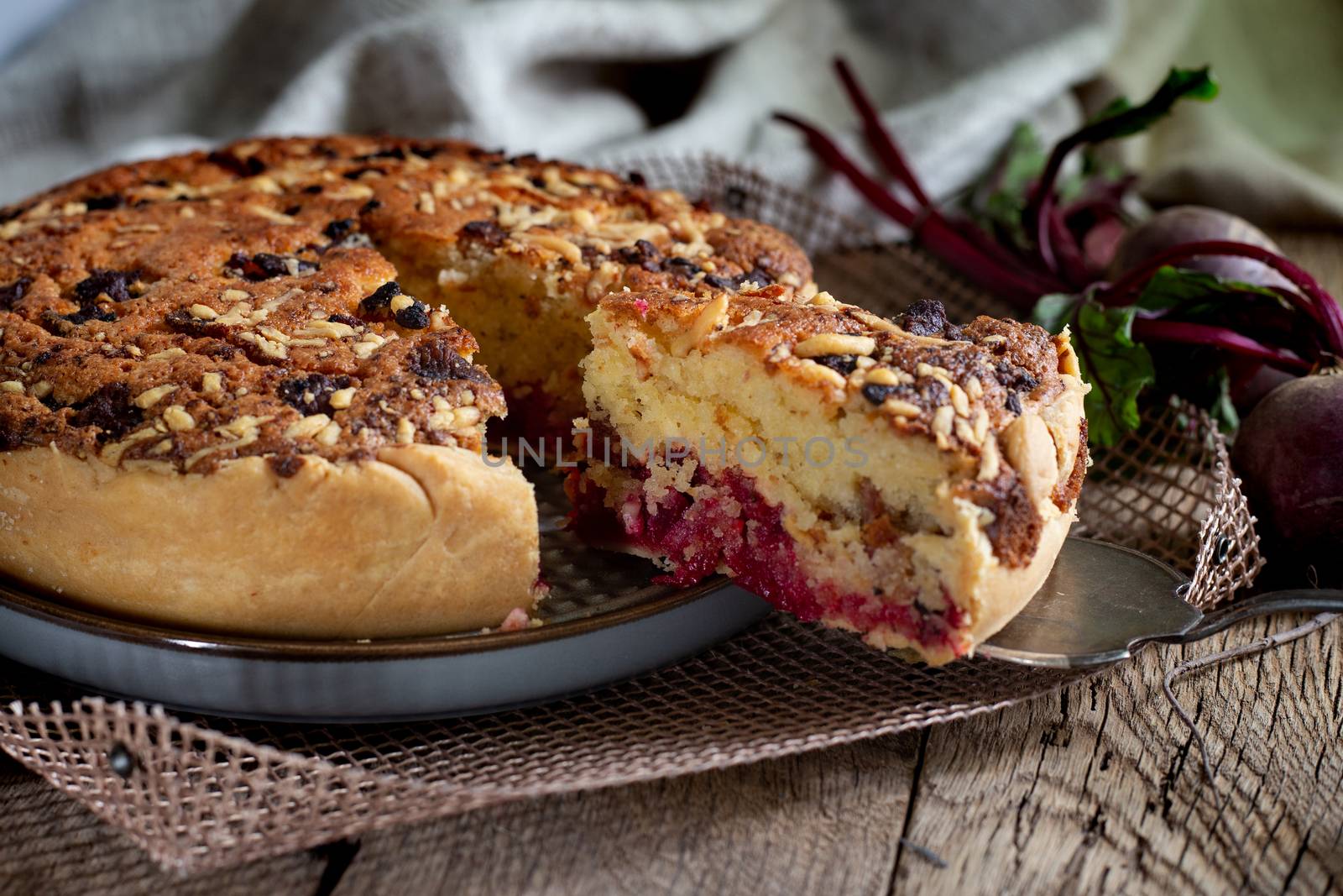 Homemade delicious beetroot pastry tart on kitchen grill with slice of cake and fresh beetroots on rustic wooden bakground. Menu, board, banner. Vintage traditional rustic kitchen. British meal