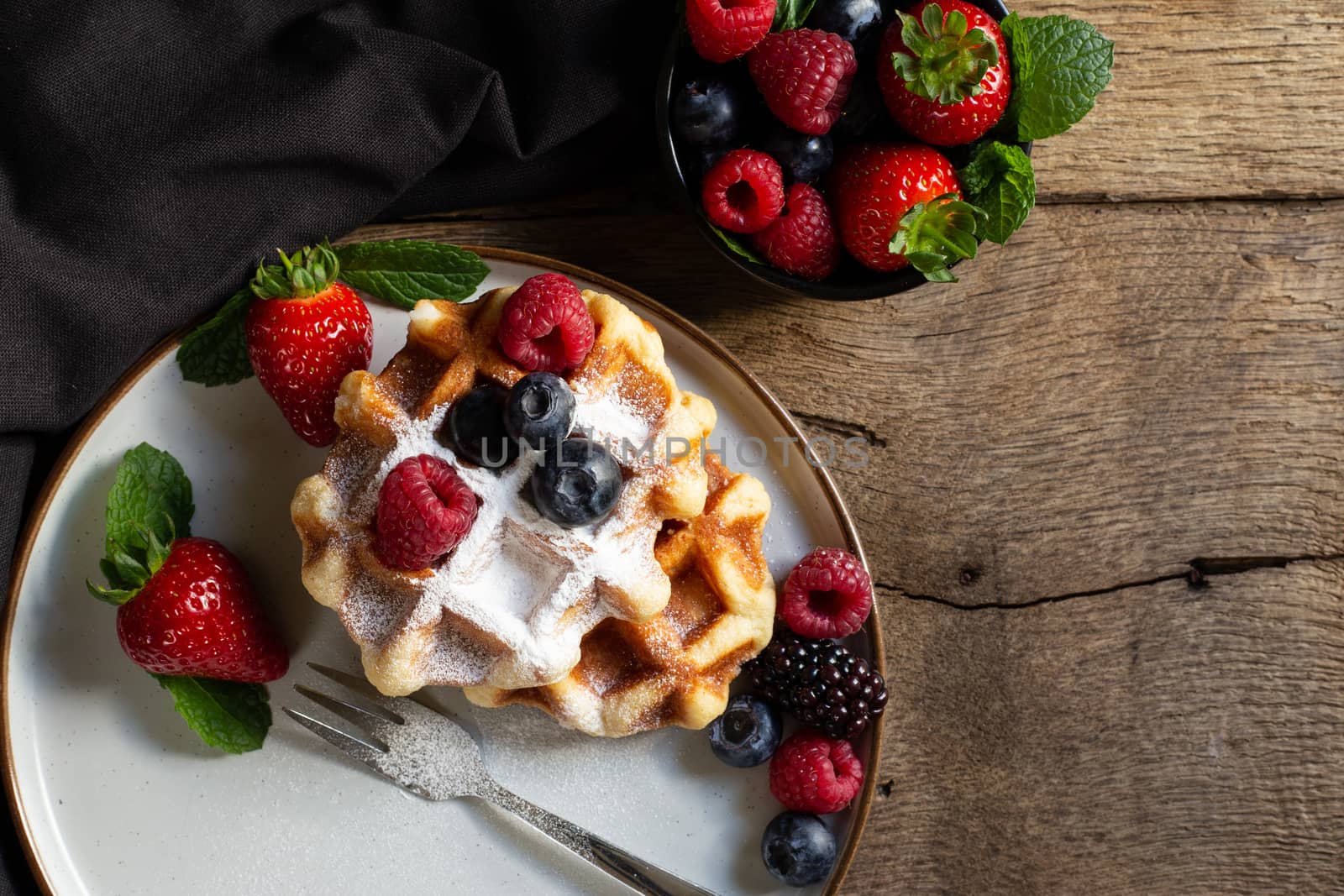 Belgian waffles with strawberries, summer berries on plate on dark old wooden dramatic background. Top view. Menu, banner, poster, mock up. Rustic vintage style of kitchen.