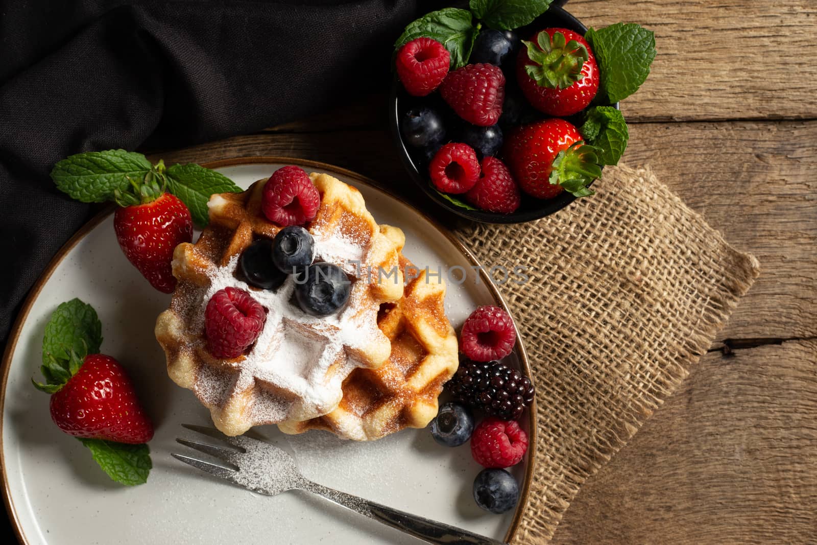 Belgian waffles with strawberries, summer berries on plate on dark old wooden dramatic background. Top view. Menu, banner, poster, mock up. Rustic vintage style of kitchen.