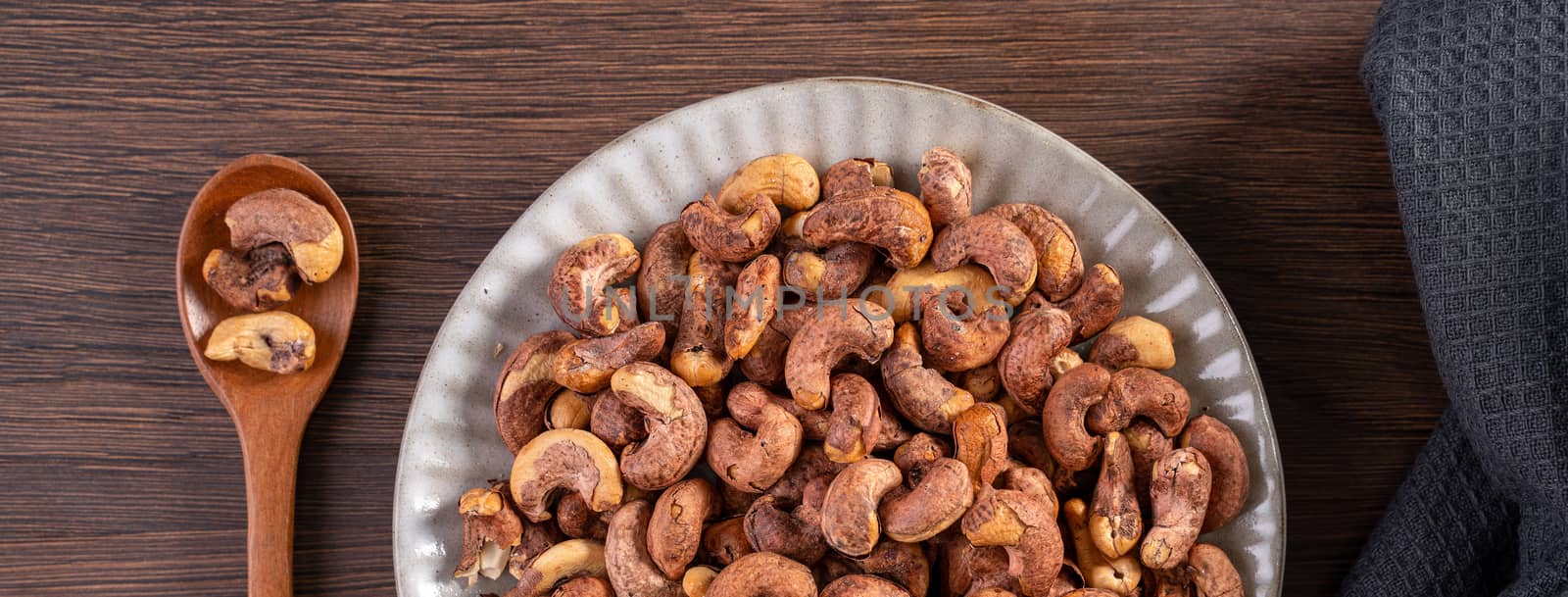 Cashew nuts with peel in a plate on wooden tray and table background, healthy raw food plate.