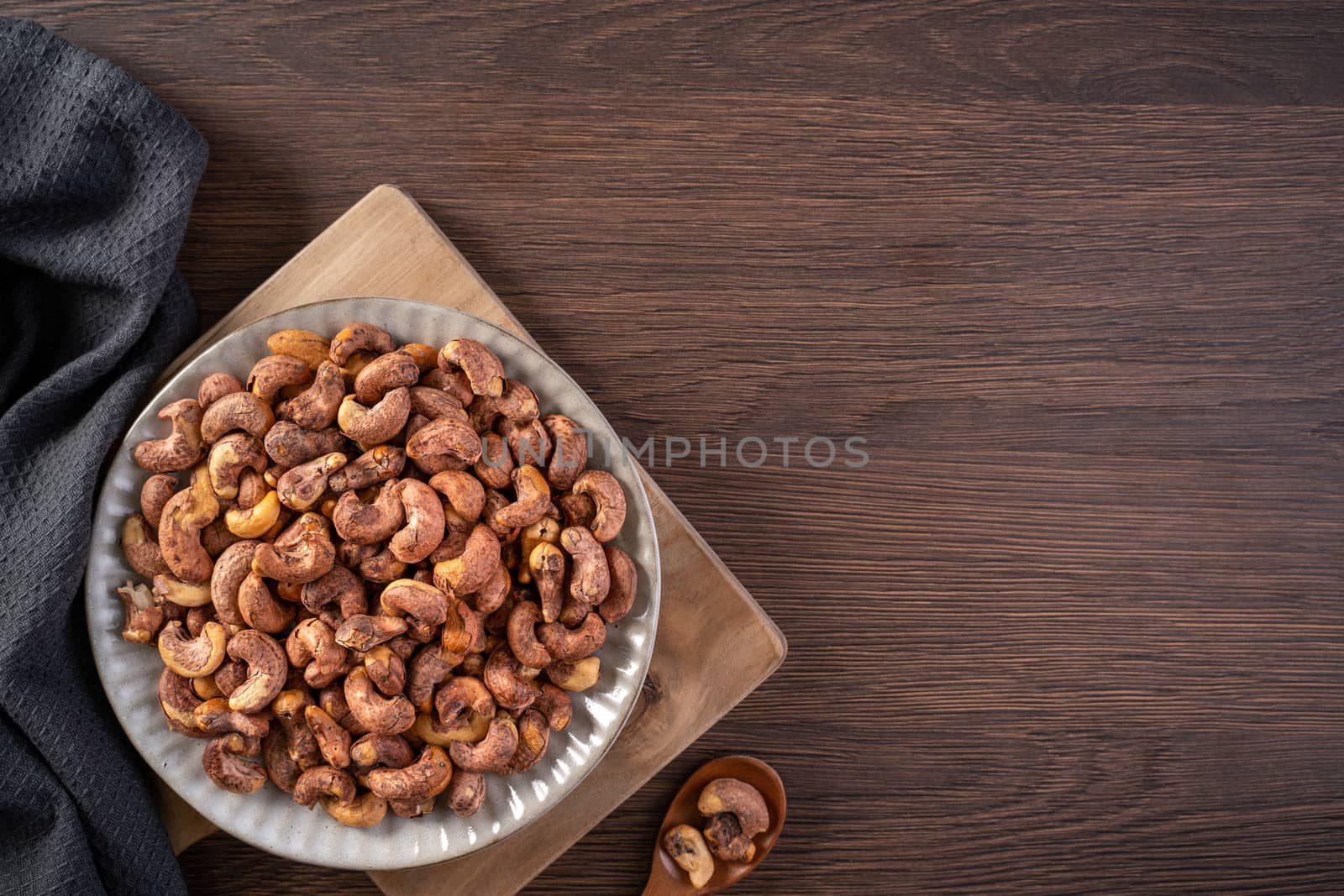 Cashew nuts with peel in a plate on wooden tray and table background, healthy raw food plate.