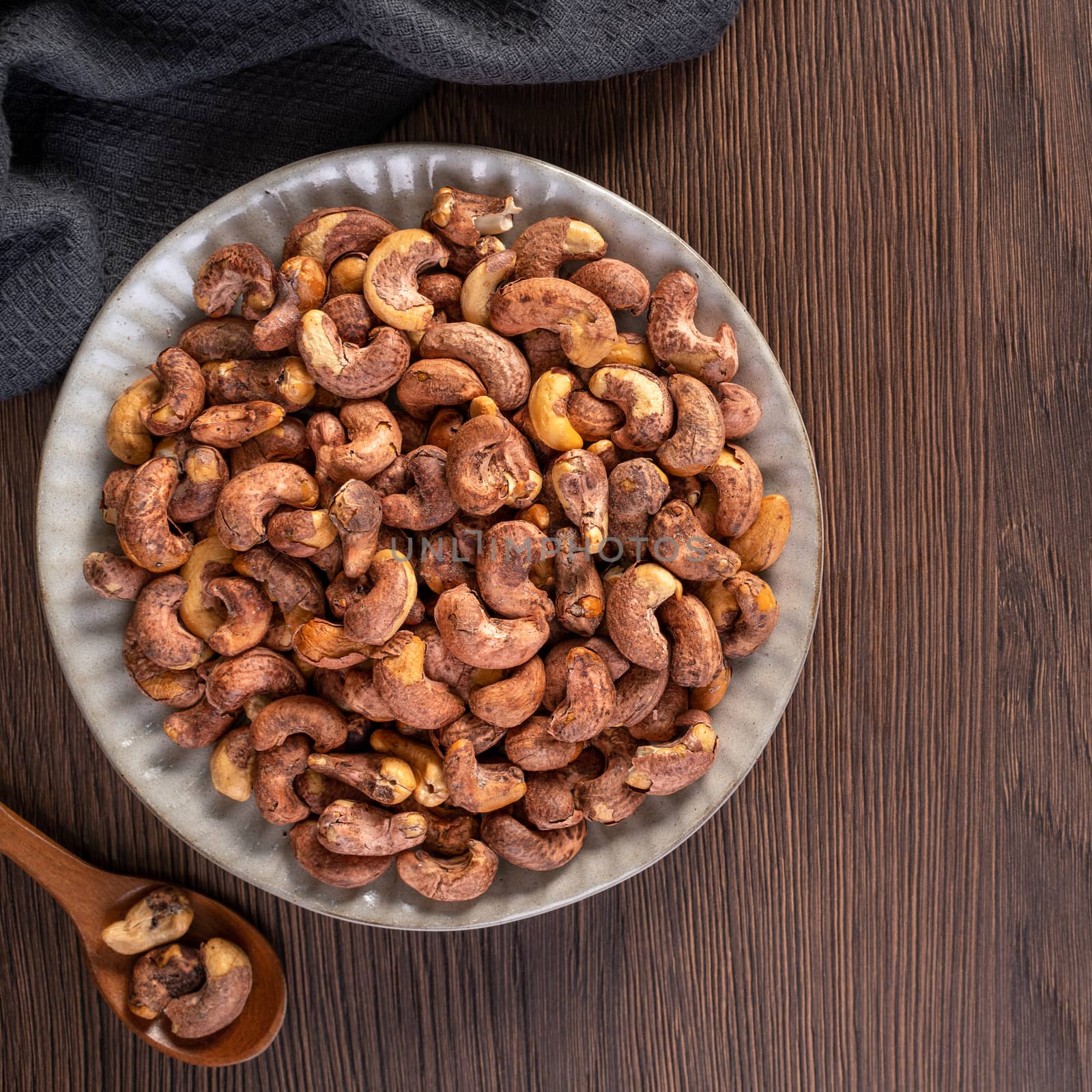 Cashew nuts with peel in a plate on wooden tray and table background, healthy raw food plate.