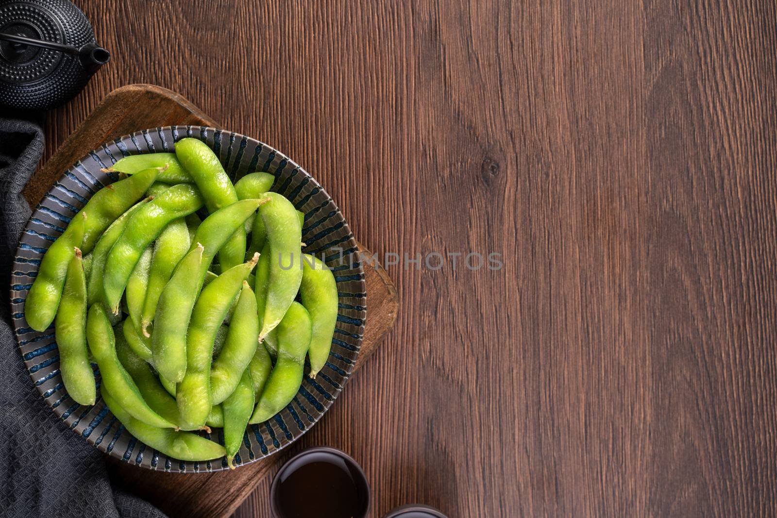 Fresh cooked boiled edamame in a plate on wooden tray and table background, healthy protein food concept.