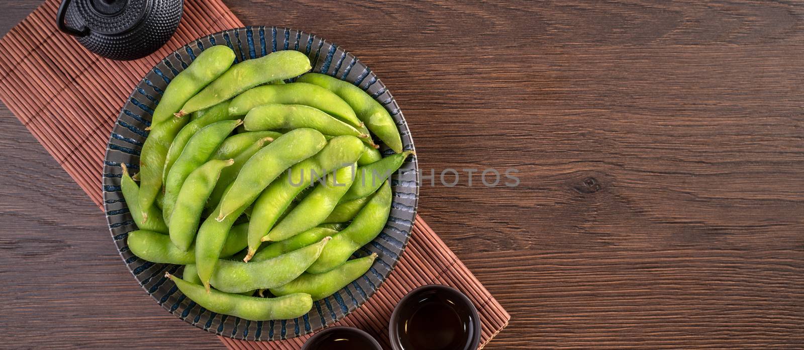 Fresh cooked boiled edamame in a plate on wooden tray and table background, healthy protein food concept.