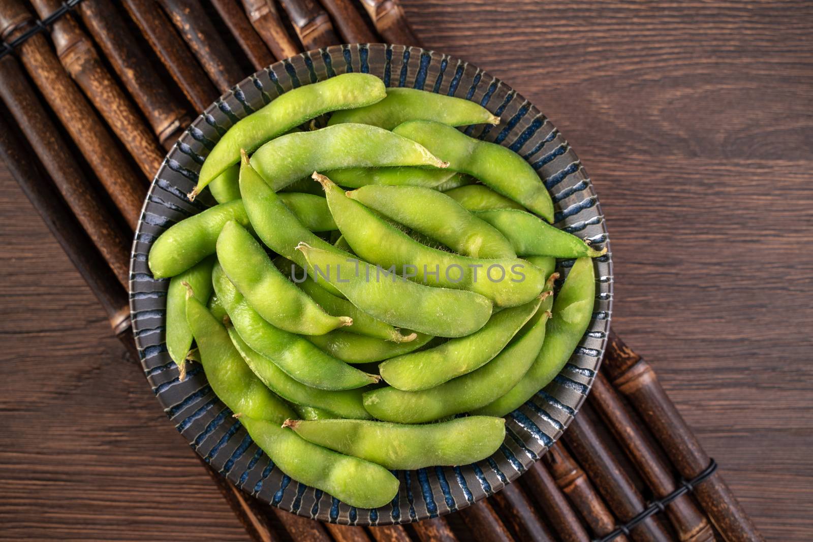 Fresh cooked boiled edamame in a plate on wooden tray and table background, healthy protein food concept.