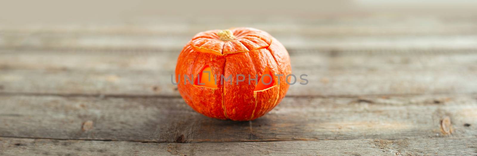 Minimalistic carved glowing Halloween pumpkin head jack lantern on wooden background with copy space gor text horizontal composition