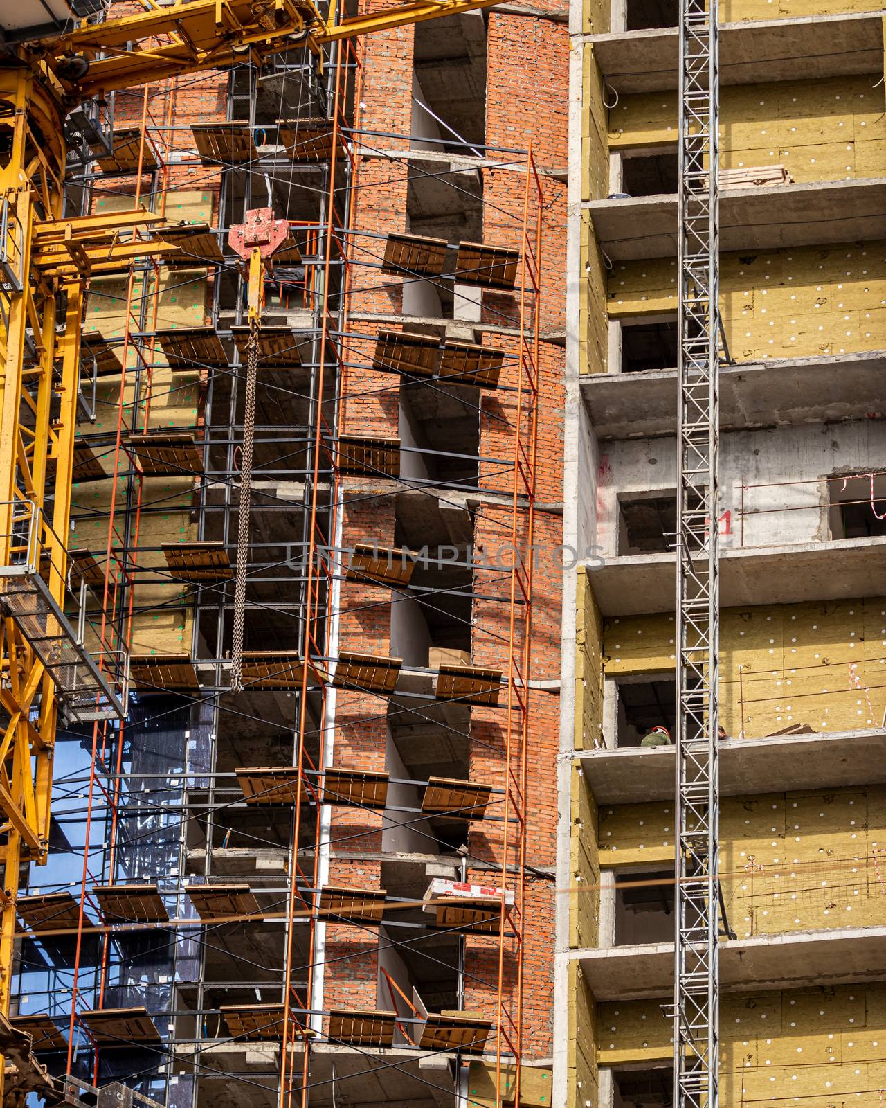 Fragment of an unfinished concrete and red brick building under construction with scaffolding and a crane.