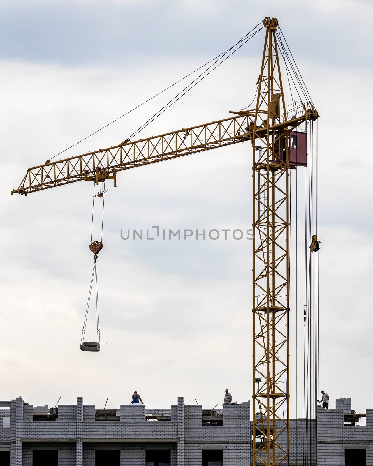 Silhouette of a team of construction workers in and a crane constructing a building on the background of the evening sunset sky.