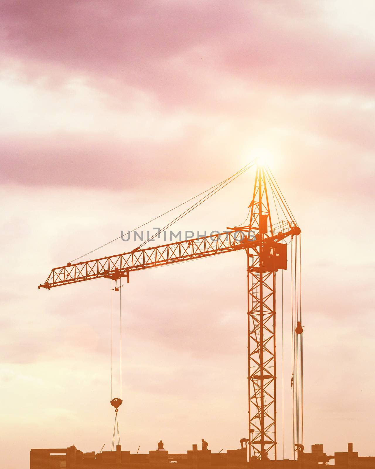 Silhouette of a team of construction workers in and a crane constructing a building on the background of the evening sunset sky.