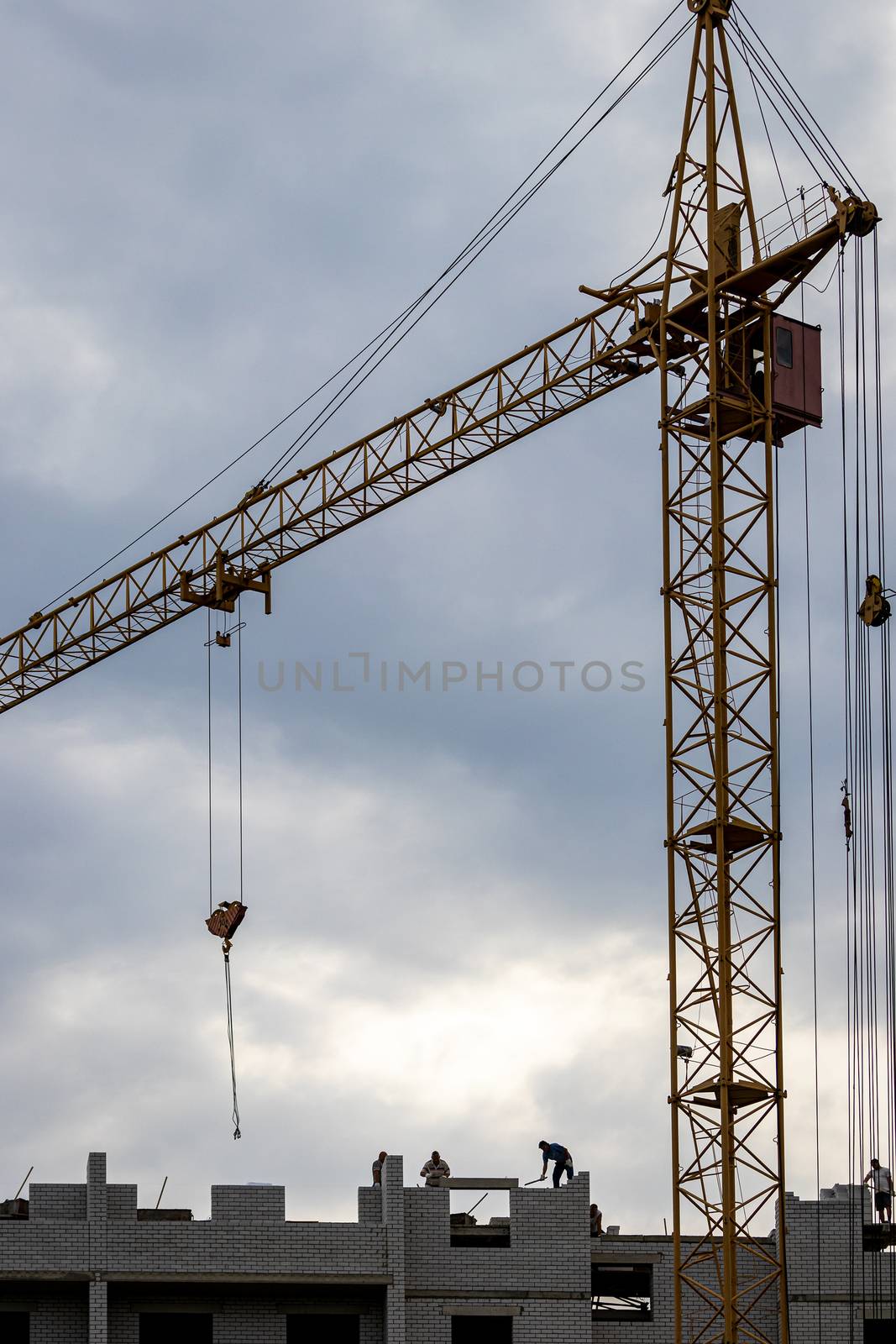 A team of construction workers in and a crane constructing a building on the background of the evening cloudy sky.