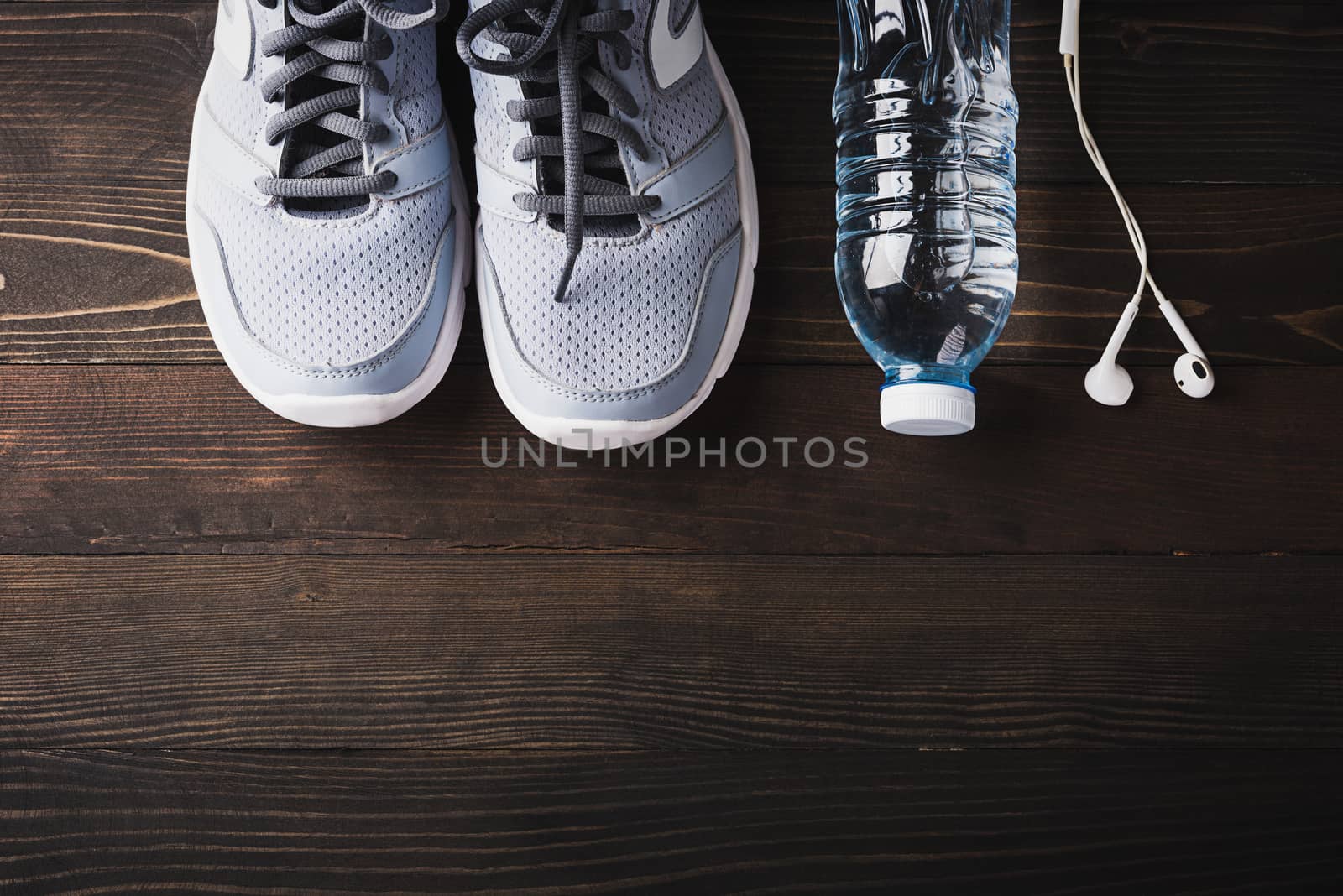 Top view of pair sports shoes, headphones and water bottle on black wood table background, Gray sneakers and accessories equipment in fitness GYM, Healthy workout active lifestyle diet concept